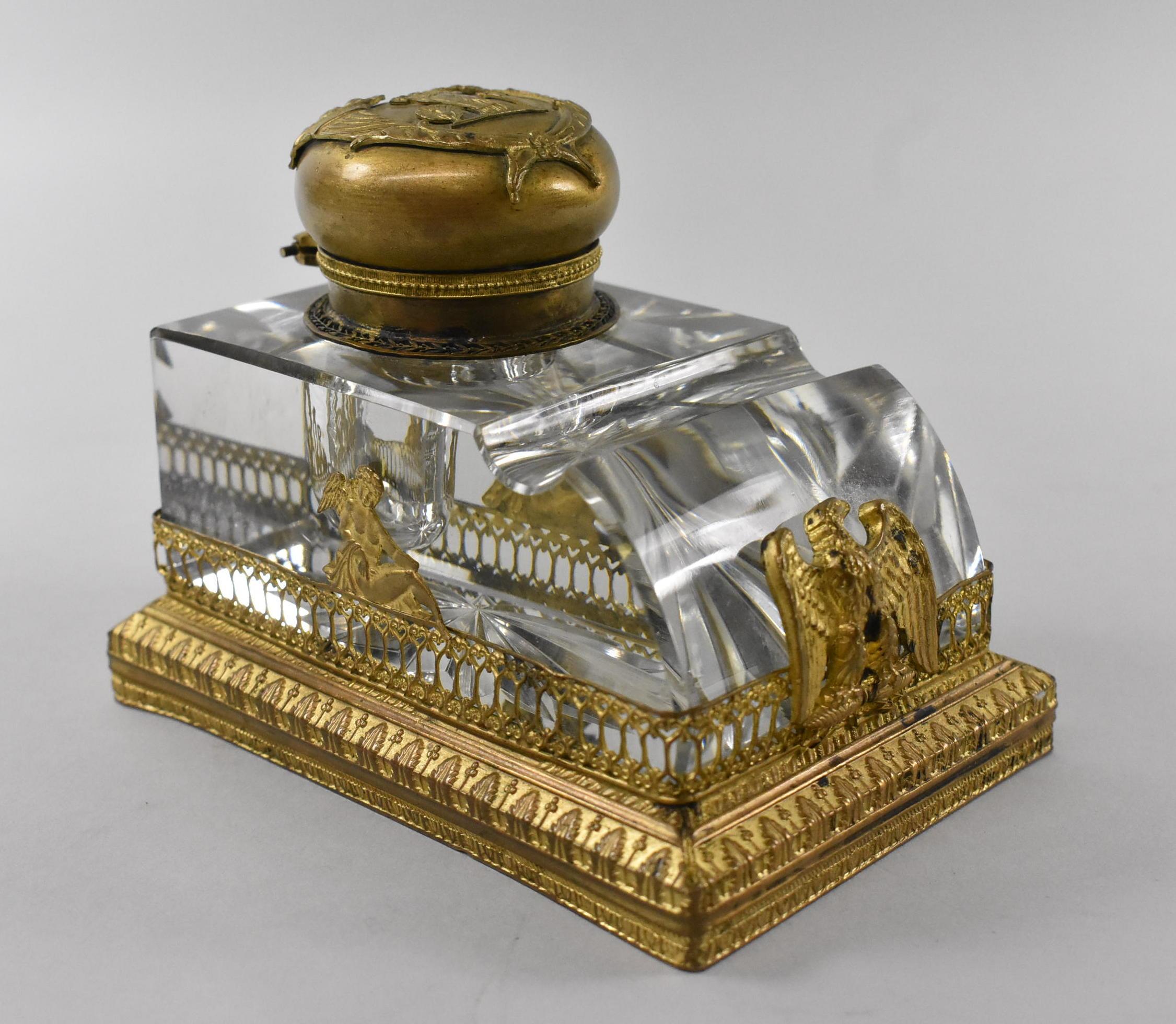 Cut glass inkwell with cut pen rest. Set in a frame of gilded gold with reliefs of eagle, cupid and wreath. Inkwell lid depicts goddess Hera holding a basket and standing next to a peacock and torch. Very good condition. Light tarnish on gold.