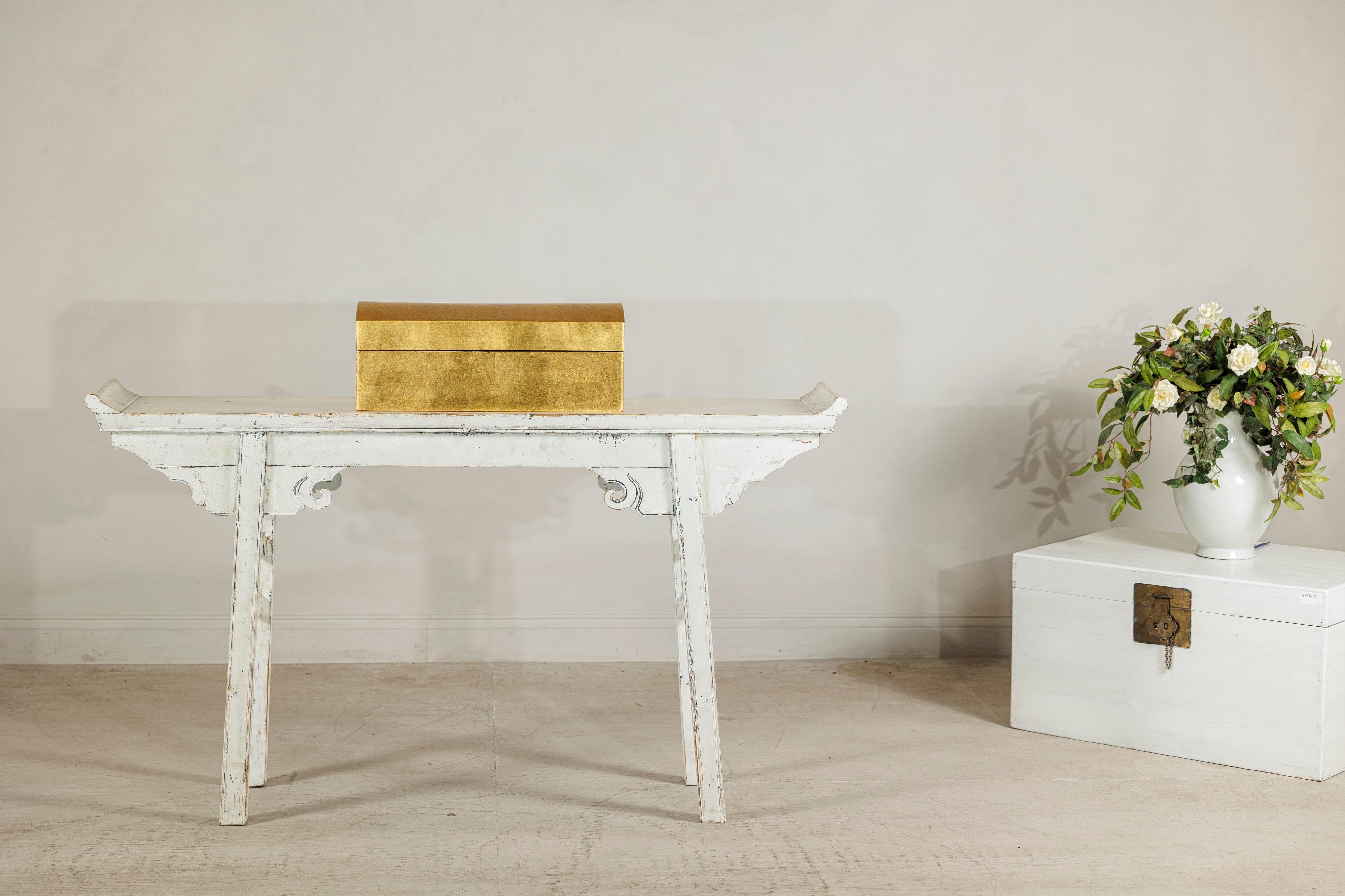 This rectangular decorative box is crafted from wood and finished in a rich gold gilt, creating a refined yet understated accent piece. The lid features a smooth, gently arched profile that echoes the shape of traditional treasure chests while