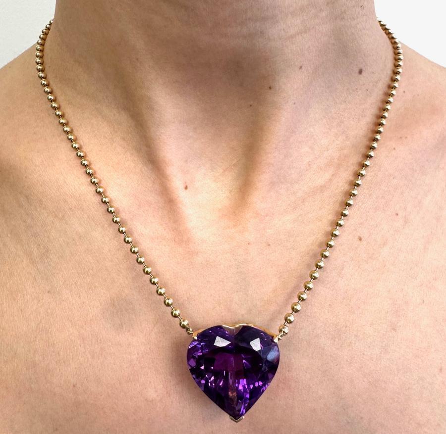 Ce collier remarquable présente une améthyste en forme de cœur de 30,63 carats sertie dans un riche or jaune 14 carats. La teinte violette profonde de la pierre précieuse et son facettage magistral rayonnent d'élégance, tandis que la chaîne à