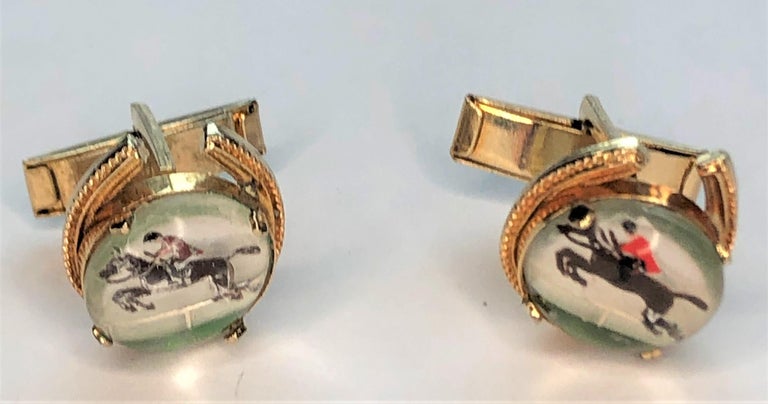 These estate intaglio cuff links are a true one-of-a-kind find!  
Yellow gold plated, decorative horse shoe shape with round, reverse intaglio.
Painted intaglio of a horse jumping with rider wearing a red shirt. 
Slight oxidation.
