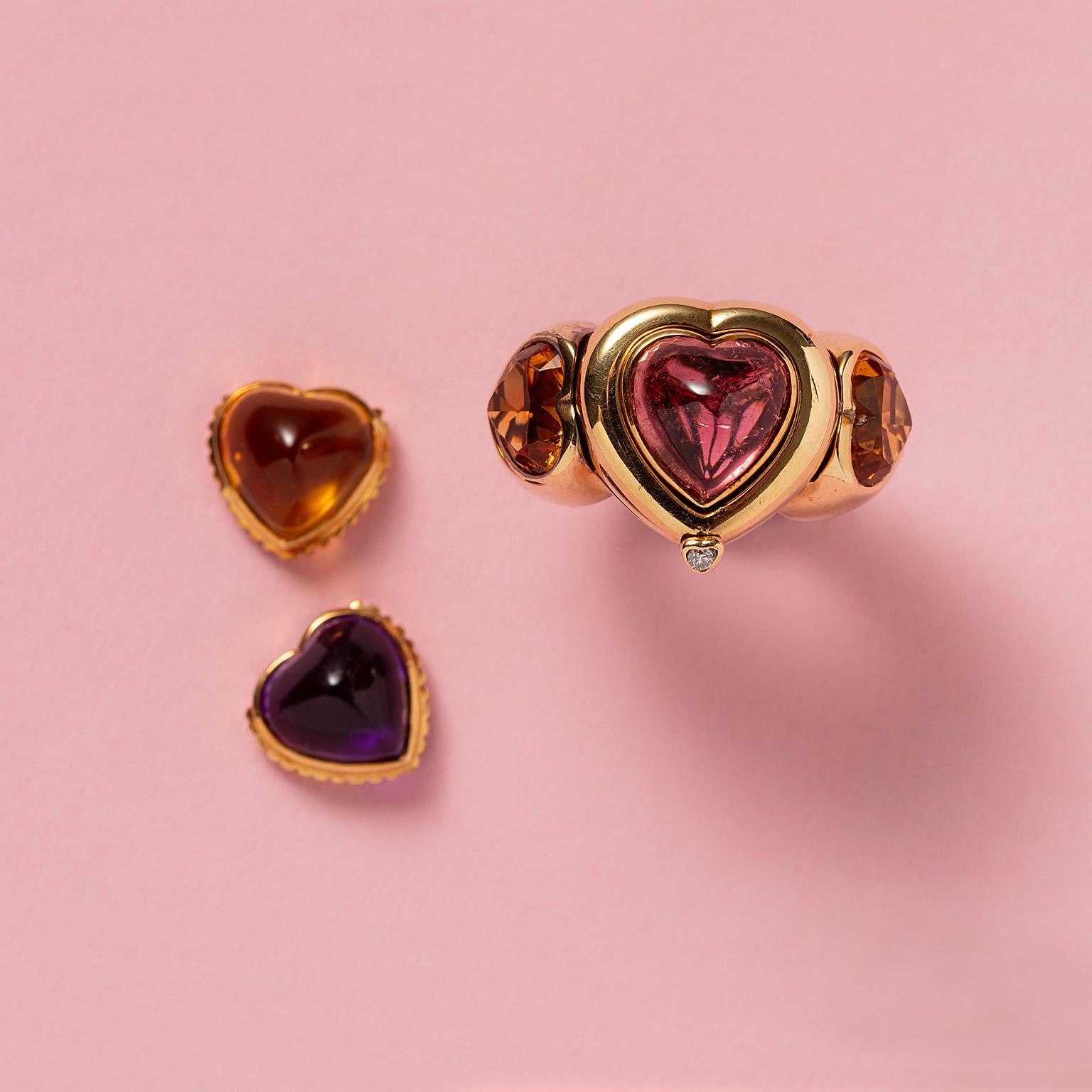 An 18 carat yellow gold heart ring with an interchangeable heart-shaped cabochon cut amethyst, pink tourmaline and citrine, a heart-shaped faceted citrine on each side, two small heart-shaped citrines at the bottom of the shank. The ring opens with
