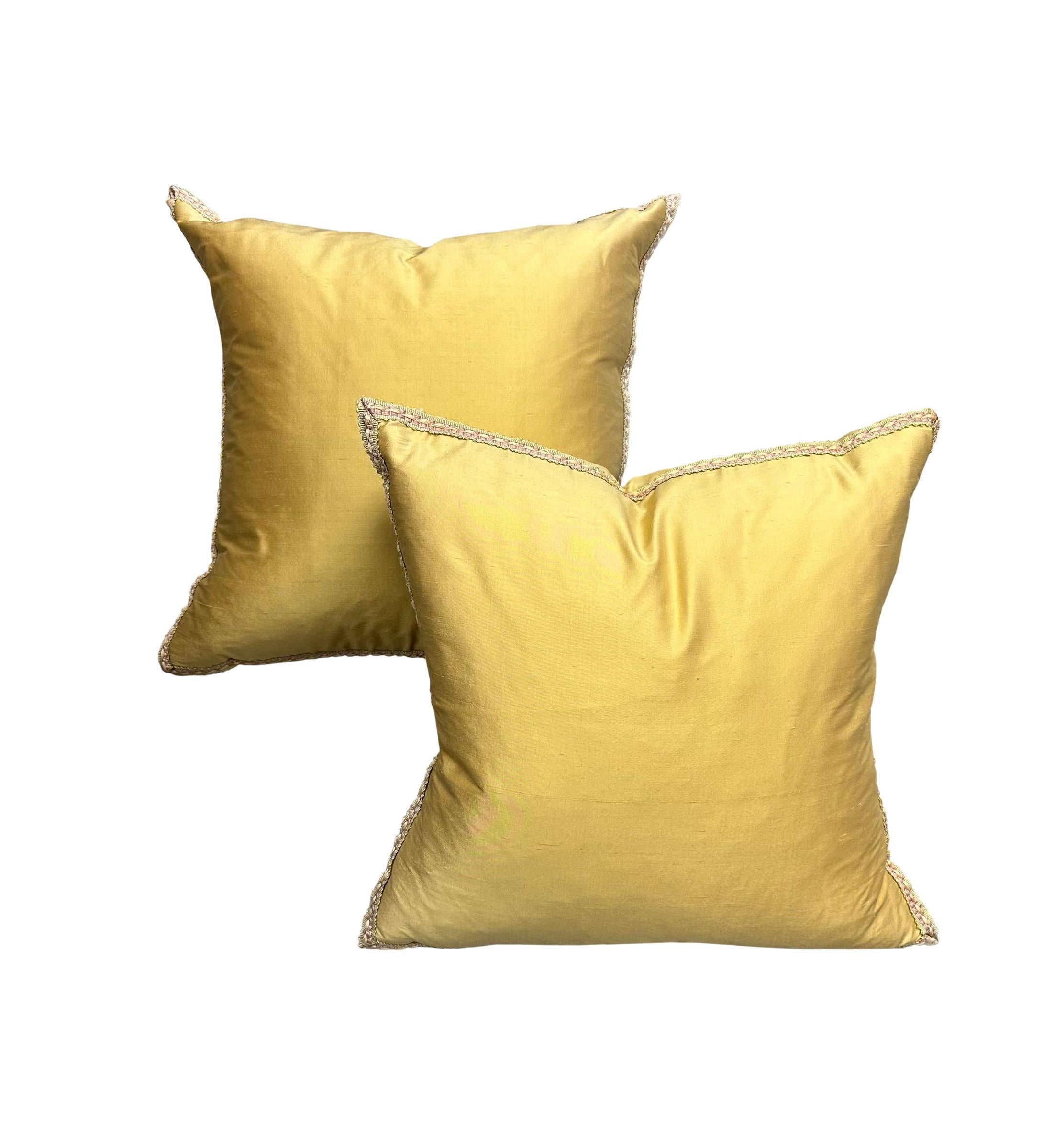 A pair of light gold silk pillows trimmed in a pink and green and yellow trim. They are the same front and back. The silk and trim are Italian, circa 1980s. The pillows are down filled.