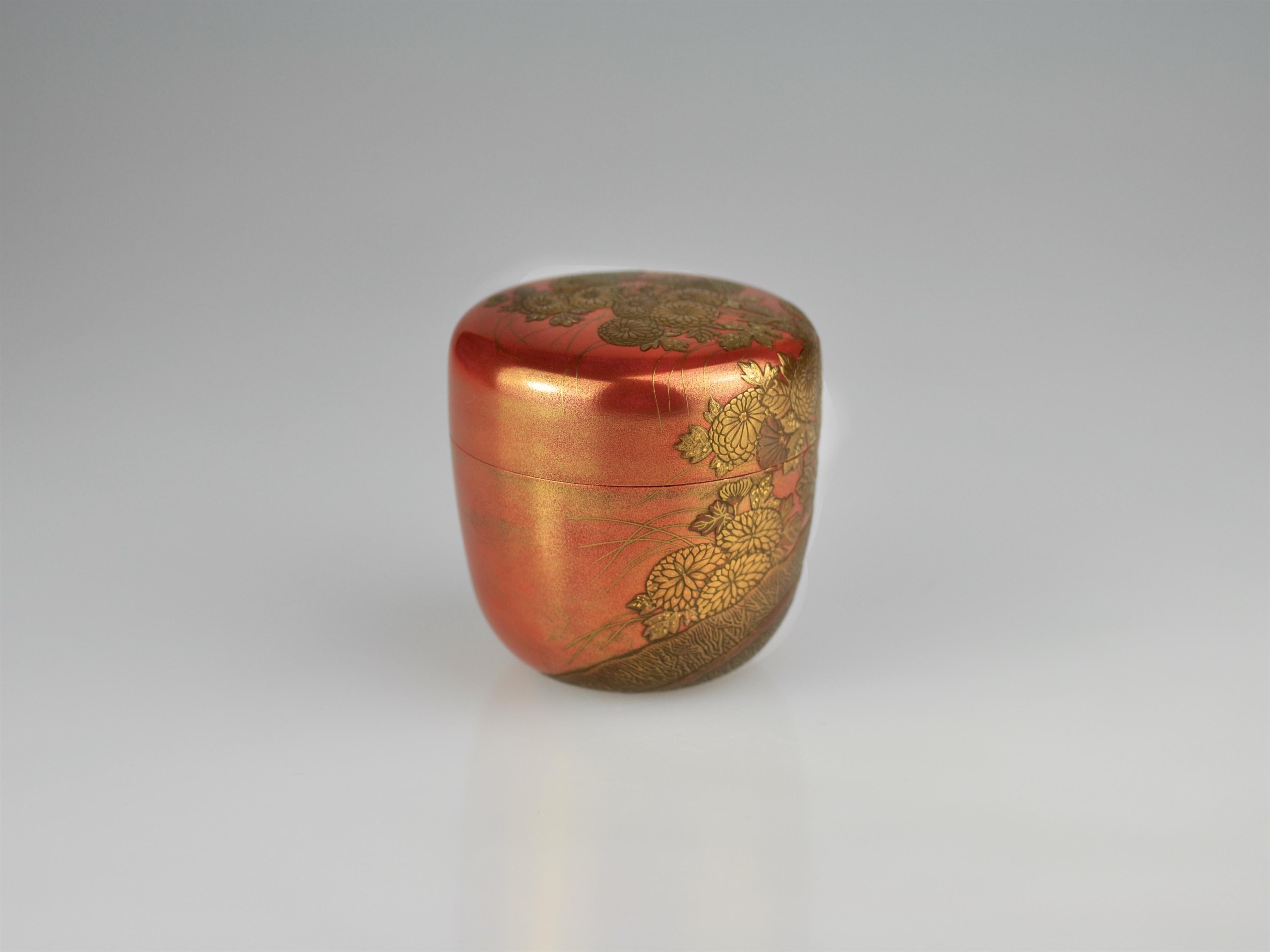 Autumn tea caddy (natsume) with a red lacquer foundation on a wooden core, sprinkled with gold powder and polished. The Classic motif of chrysantemums flowering on a bambus fence is applied in takamaki-e. The image usually refers to the famous 