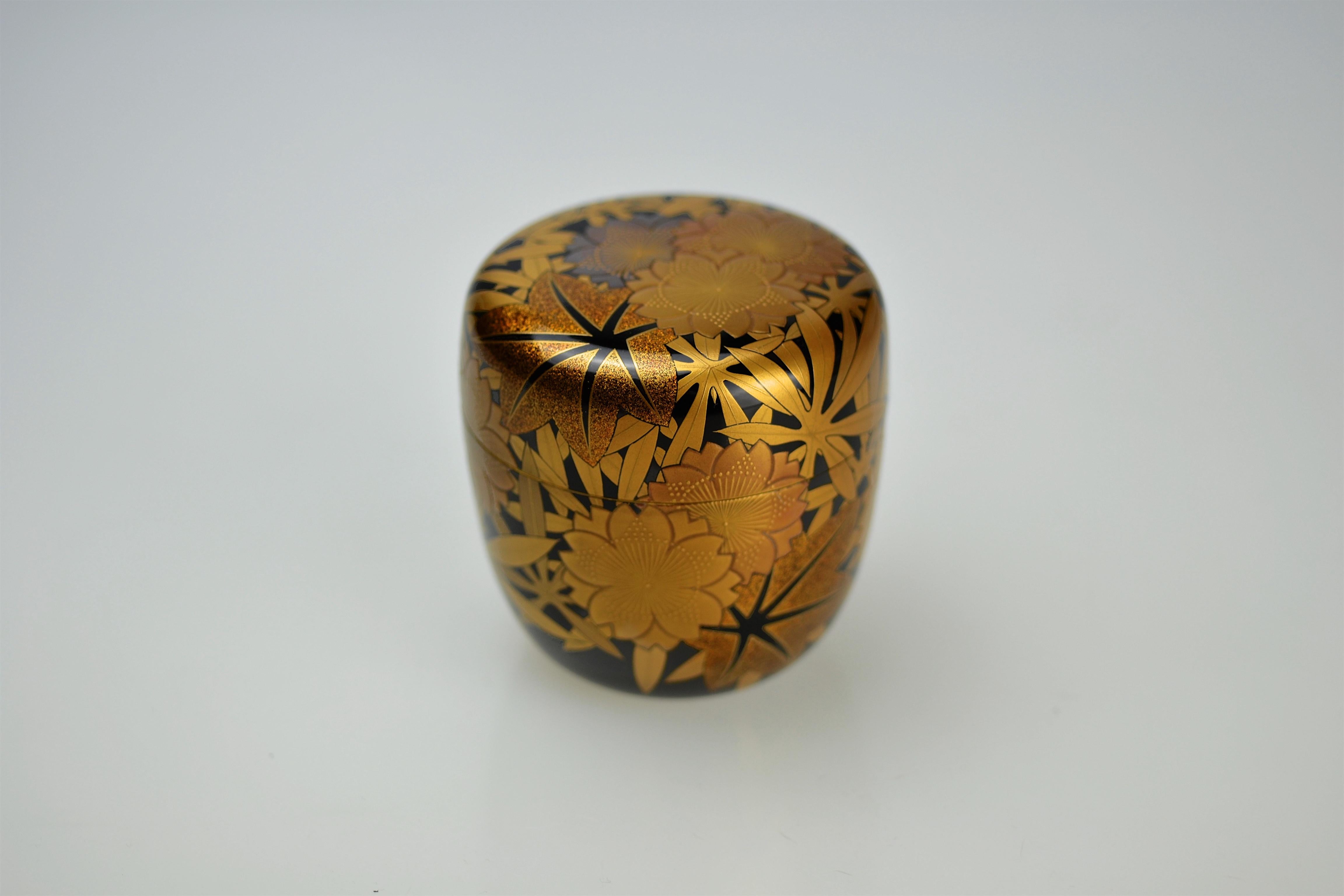 Luxuriously decorated tea caddy (natsume) made by Kakinoki Akira (1926-2009). The exterior is finished in polished black lacquer (roiro) and elaborately decorated with gold and silver takamaki-e camellia blossoms and sprinkled (nashiji) marple