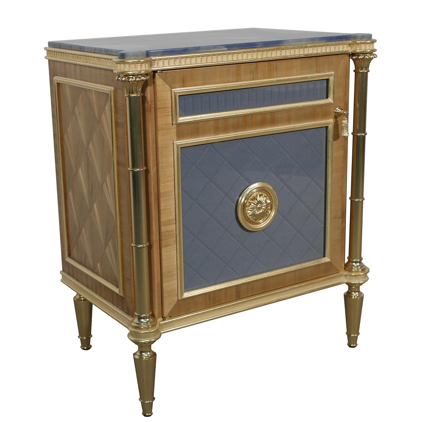 This one-door wooden bedside table boasts a glossy finish and natural straw veneer accents. Complete with one inside drawer, the design is enhanced with brass details, flaunting a 22-karat gold-plated finish. The 22-karat gold leaf accents feature a