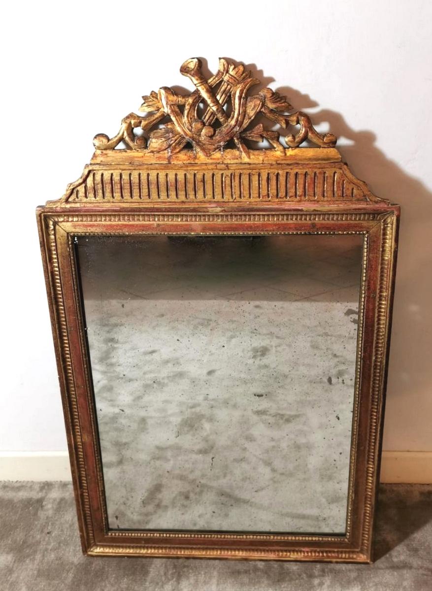 Elegant wooden frame with mirror produced in France in 1750 Louis XVI; on the upper side, we find a rich carved ornament representing two musical instruments, a lyre, and a flute, tied together by a floral decoration, while the sides of the mirror