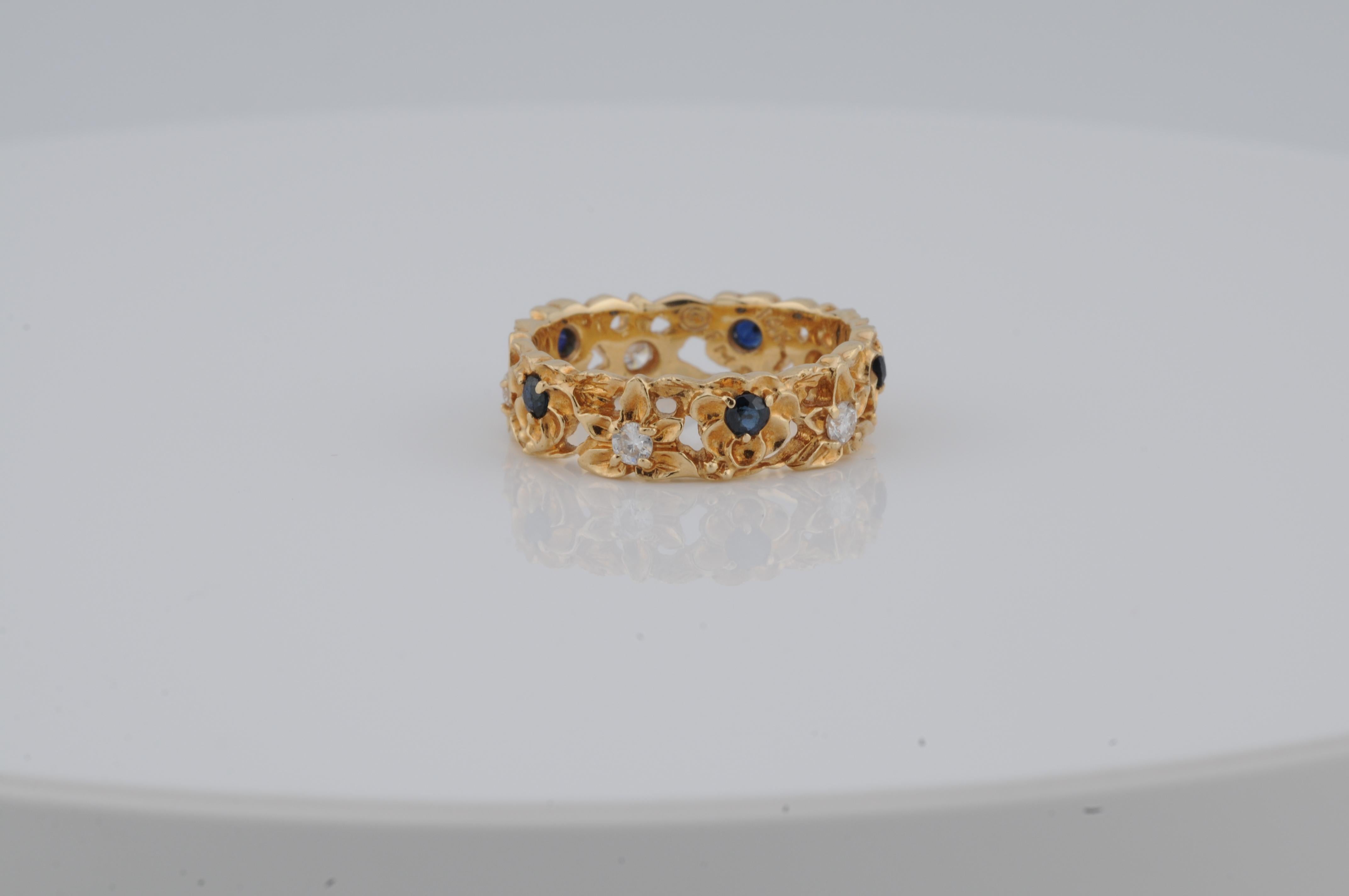 Anello con memoria floreale in oro giallo 14K, con diamanti e zaffiri incastonati. Il design dell'anello ha la forma di un fiore stilizzato, con le pietre che rappresentano i petali e il centro. I diamanti e gli zaffiri sono incastonati in modo