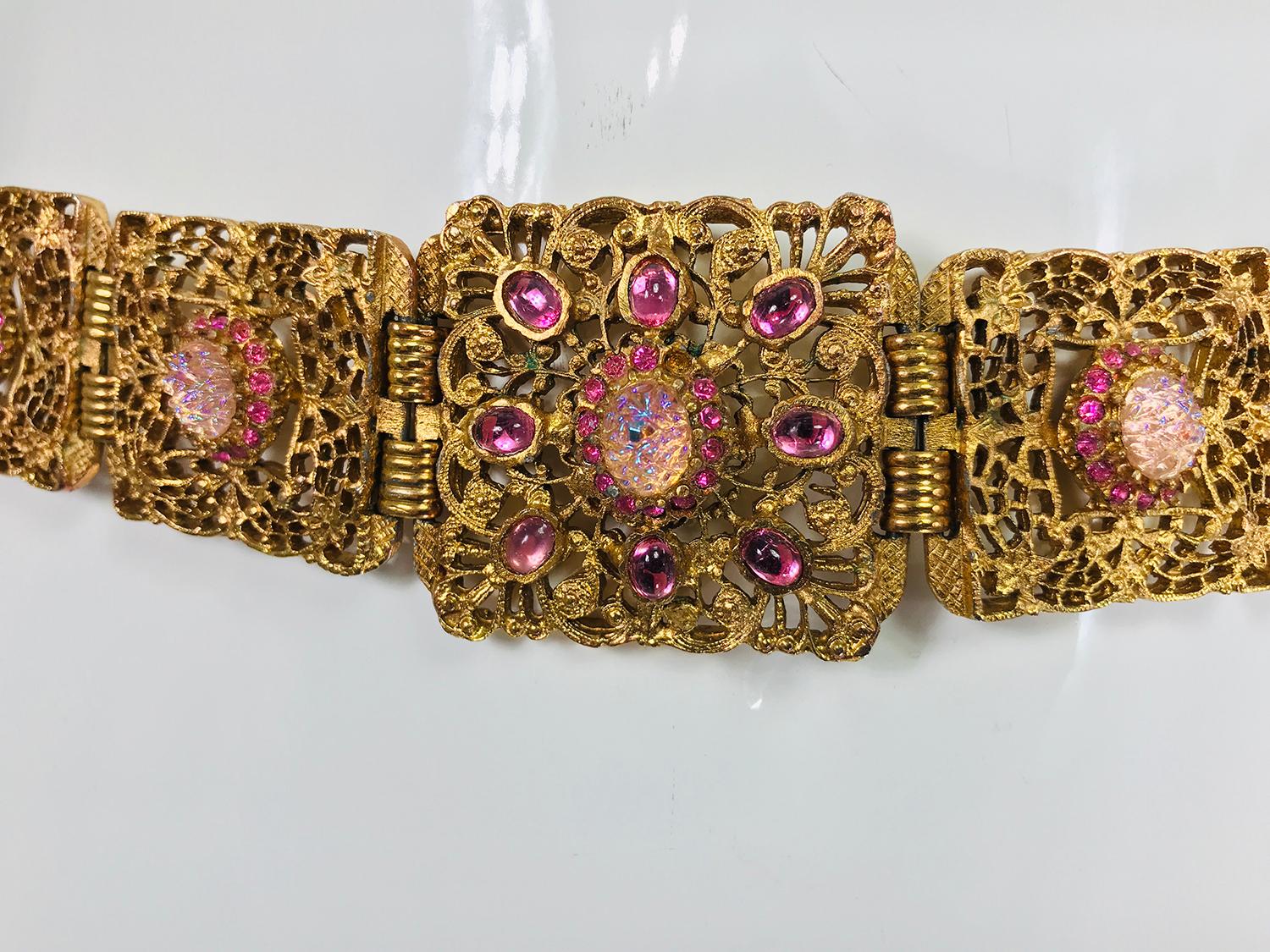 Gold metal filigree link belt with pink textured glass ovals and faceted rhinestones from the 1960s. This beautiful belt closes with a hidden hook at the side. The front of the belt features a square link, the other links are rectangular, all with