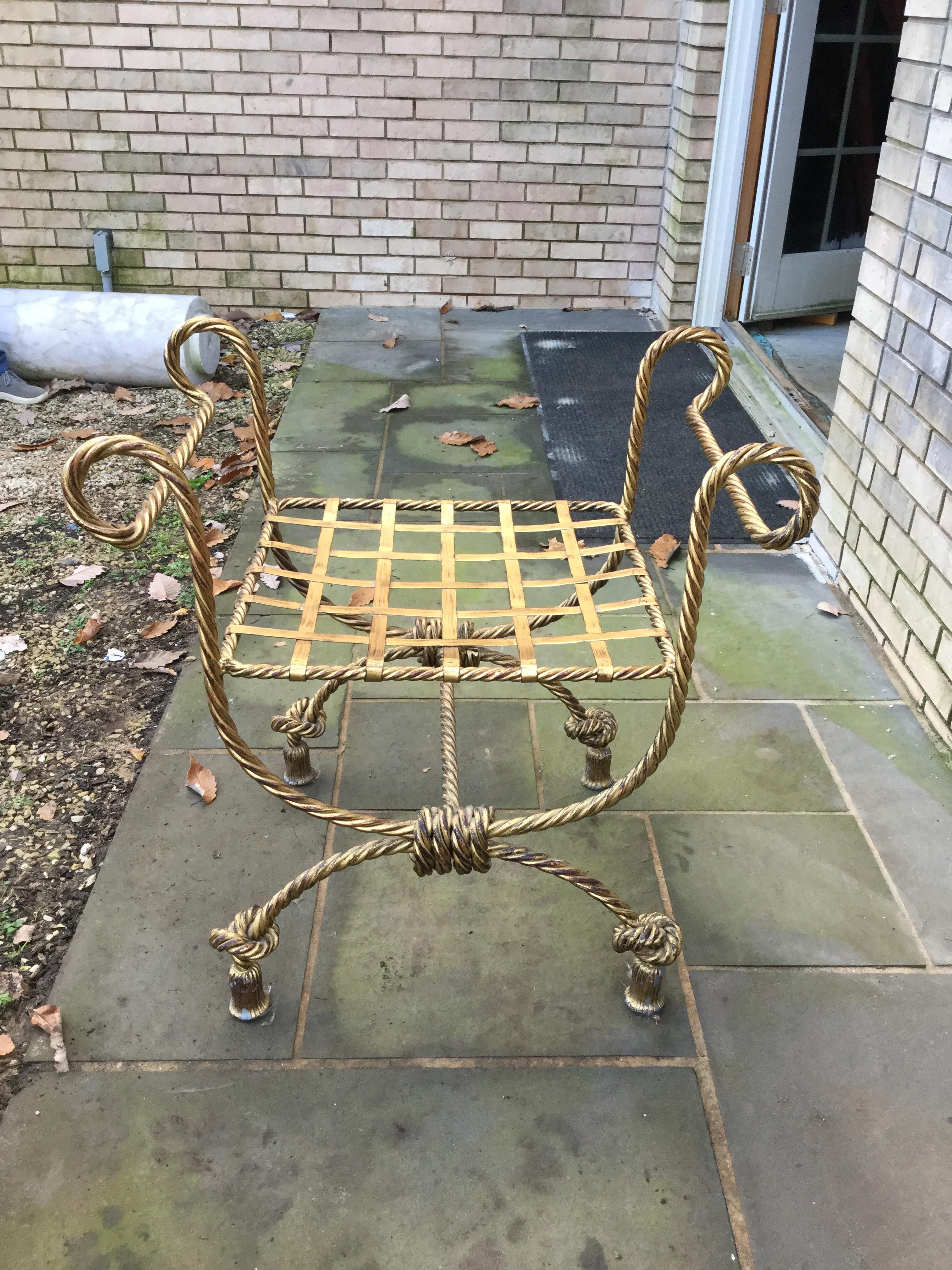 Elegant and decorative gold metal bench. This bench features a rope design throughout with the feet finishing in a knot and tassels. Highly desirable in a bathroom or powder room. Excellent condition.