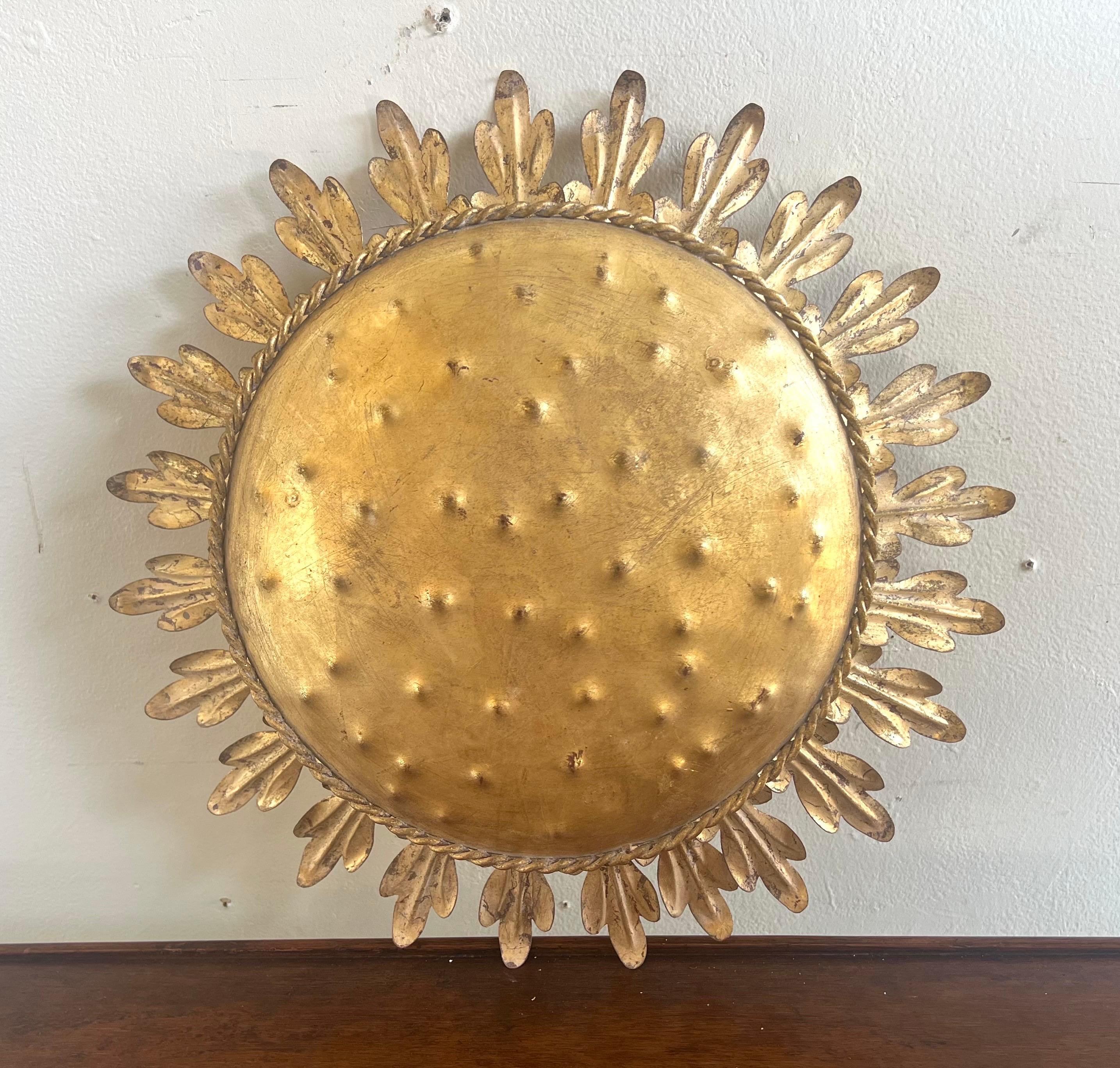 Plafonnier personnalisé en métal doré avec un motif en forme de soleil.  Le luminaire présente une plaque centrale ronde en métal martelé avec une bordure en forme de corde.  Autour de la plaque centrale, des bras métalliques rayonnent vers
