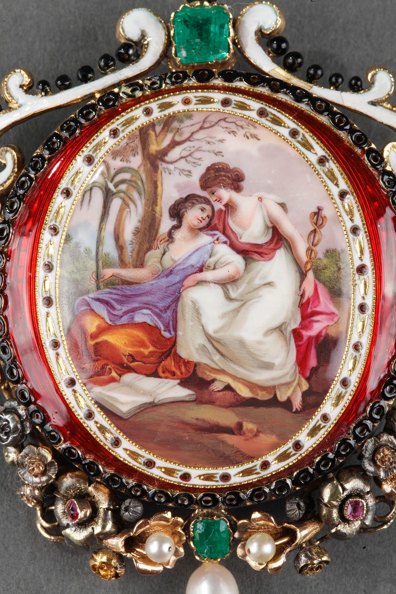 Ovale Goldbrosche mit einem Medaillon aus Emaille, das zwei weibliche Figuren in einer Landschaft zeigt.  Jede von ihnen trägt ein Attribut, das mit der Mythologie zusammenhängt.
Die durchbrochene Fassung mit floralem Motiv wird durch einen