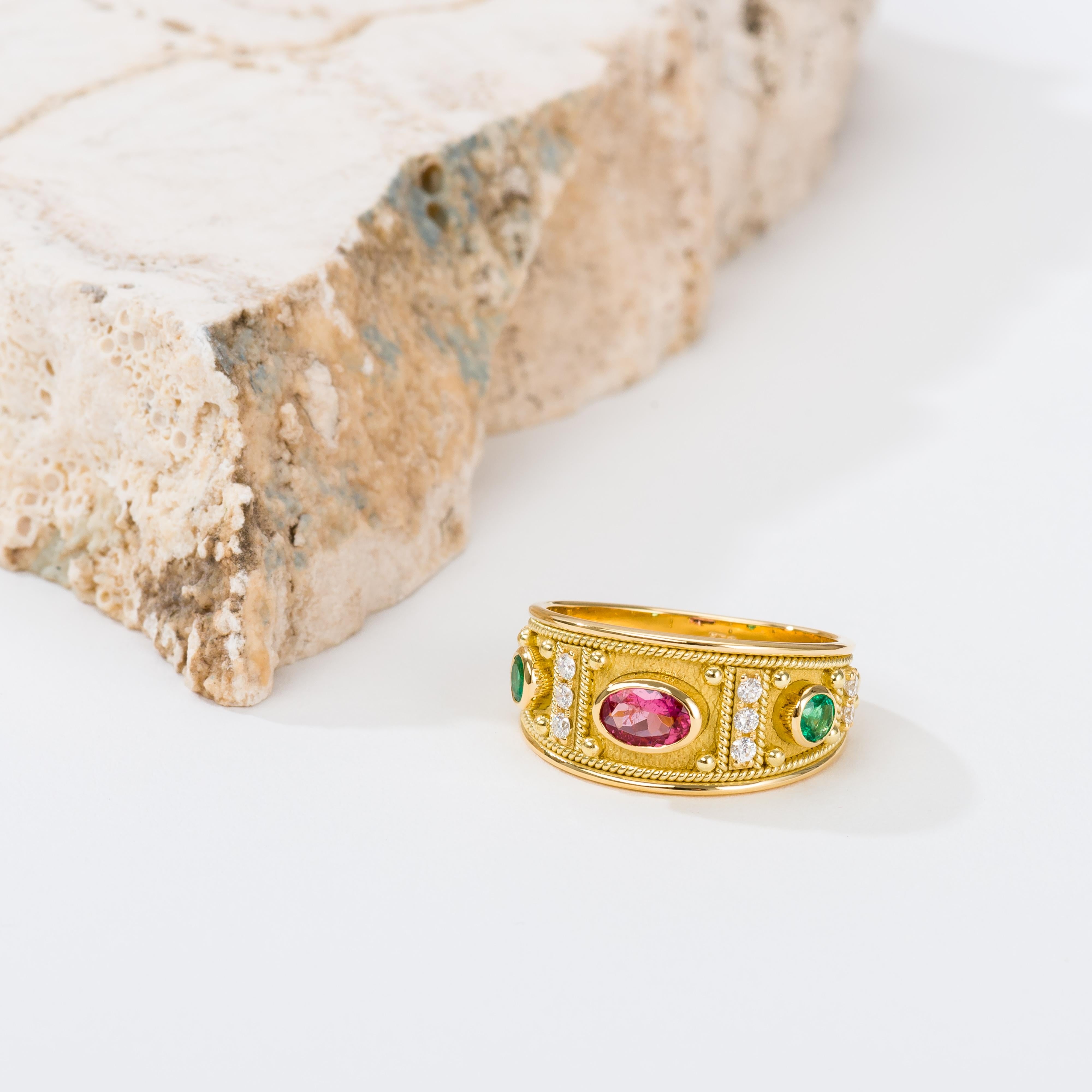 Admire the enchanting beauty of a gold ring, graced by a captivating oval pink tourmaline, surrounded by two rows of sparkling diamonds, and adorned with two round emeralds—an exquisite fusion of color and brilliance that adorns your hand with
