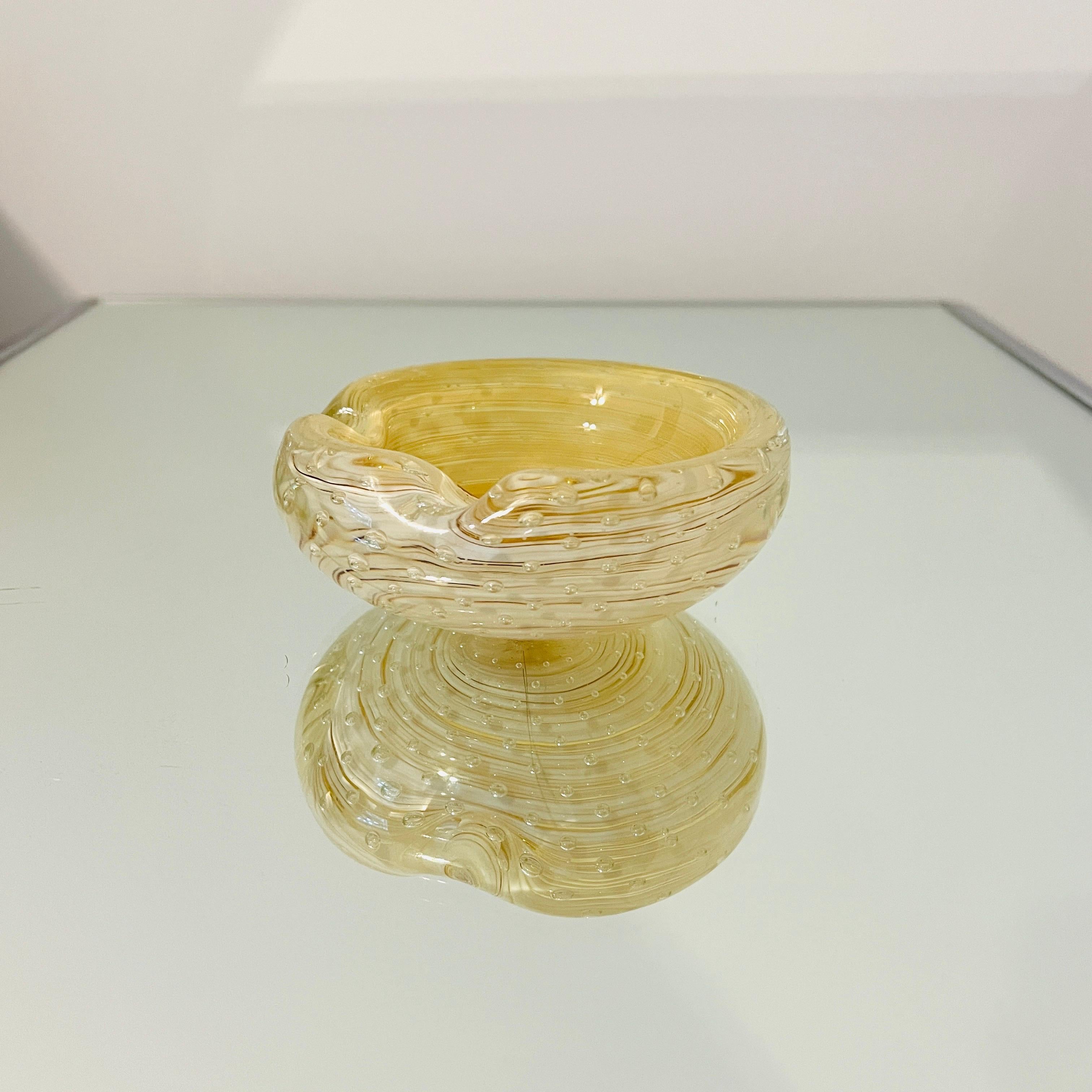 Ciotola o posacenere di Murano fatto a mano con macchie d'oro e design a bolle controllate.  La ciotola presenta la tecnica del sommerso con volute di vetro bianco tra l'oro.  È un oggetto decorativo chic. 