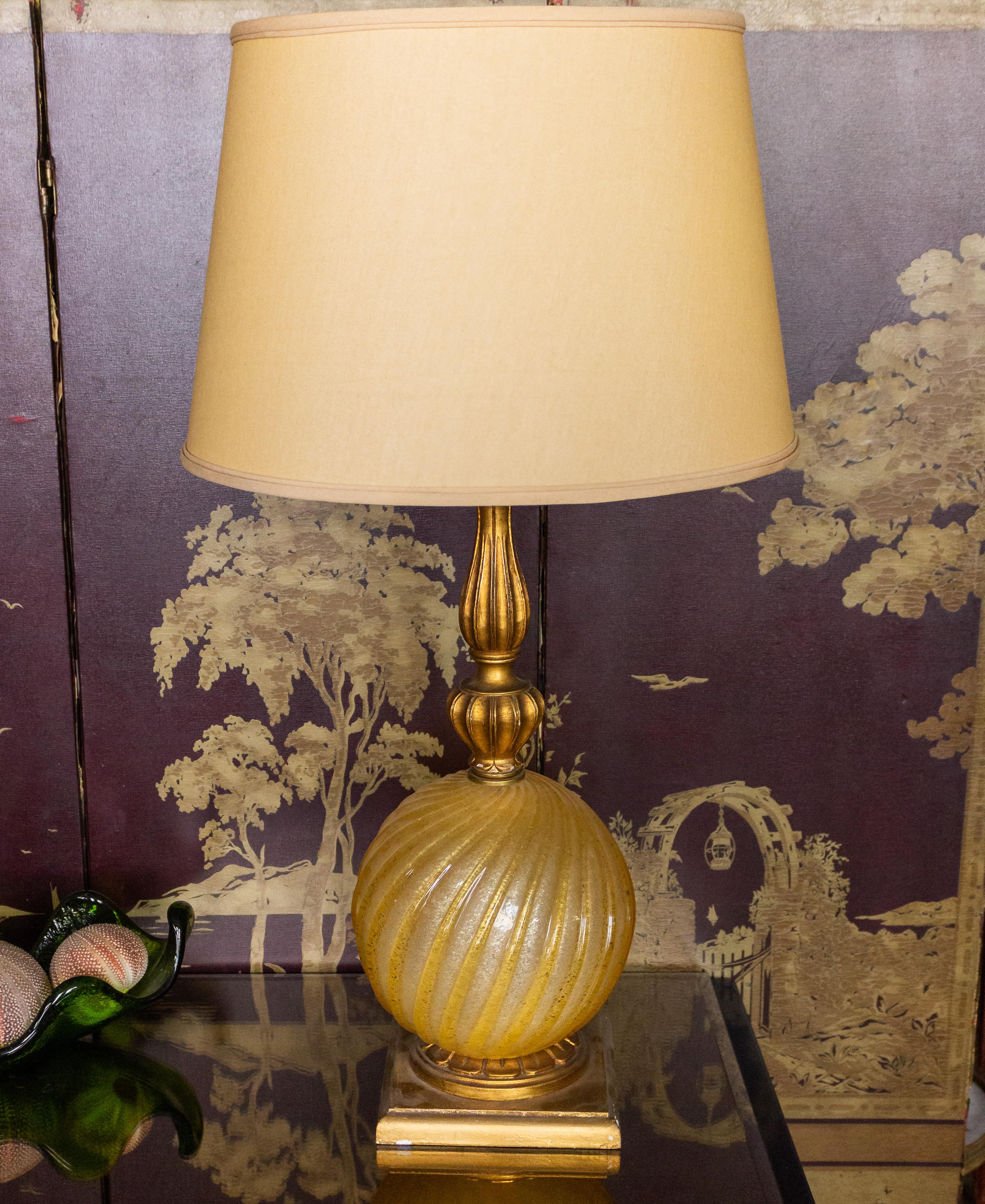 Une superbe lampe de table globe en verre Murano doré avec une tige et une base en bois doré méticuleusement détaillées. Cette élégante lampe a été récemment recâblée, ce qui garantit sa fonctionnalité pour les années à venir. Bien qu'il soit en bon