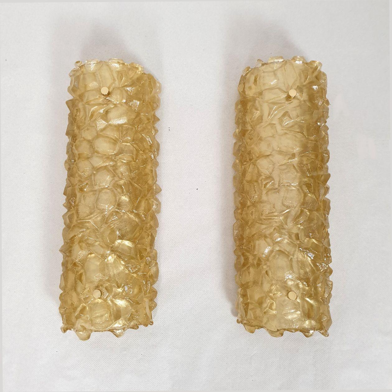 Pair of Mid Century Modern Murano glass sconces, Mazzega style, Italy 1980s.
The pair of sconces is made of a thick piece of golden yellow Murano glass, with an irregular surface.
The glass is translucent.
The back plate is painted white and the