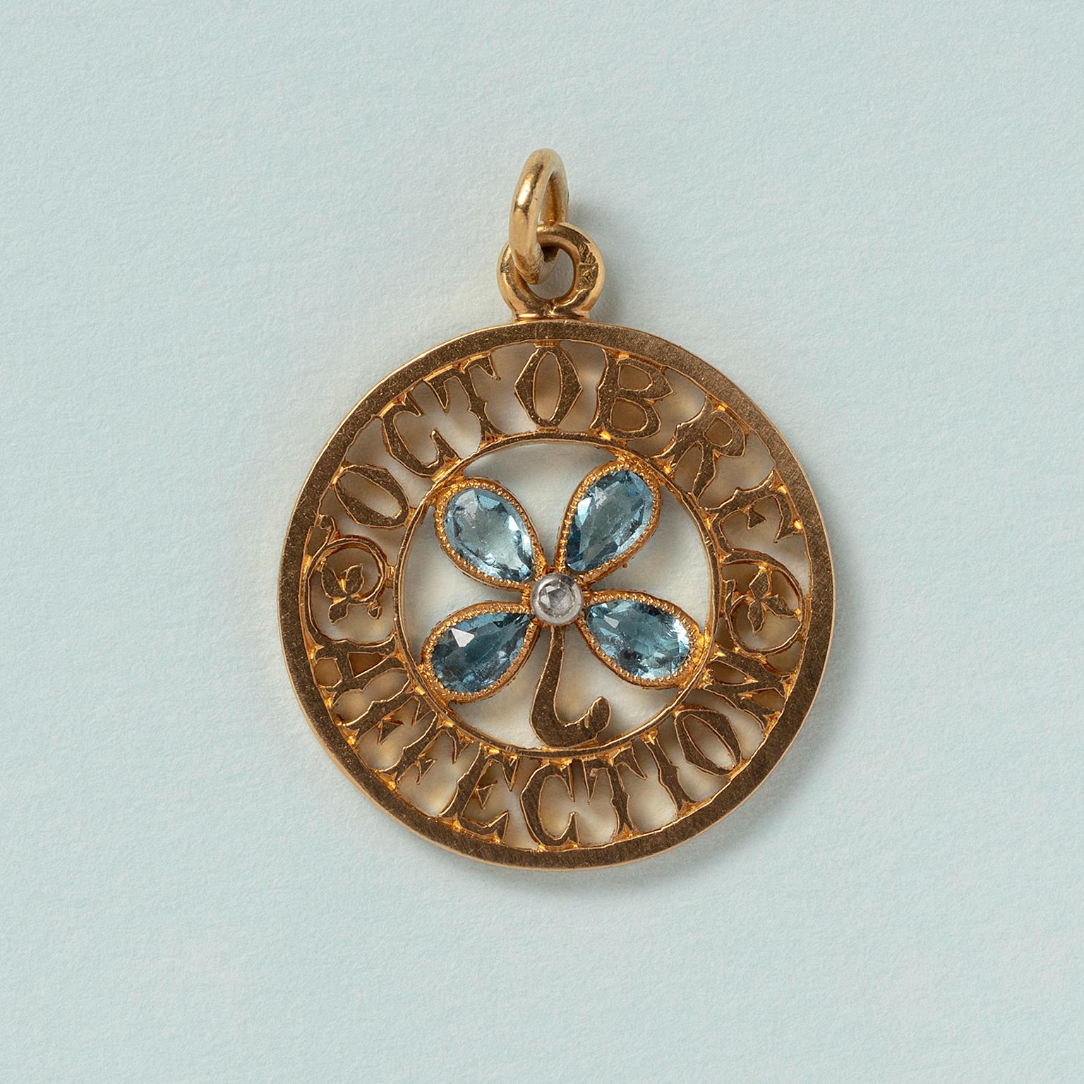 An 18 carat gold charm with a clover four with aquamarine petals and a diamond heart with the text 'Octobre Affection', France circa 1910.

weight: 3.8 grams
dimensions: 2.4 x 2.0 cm