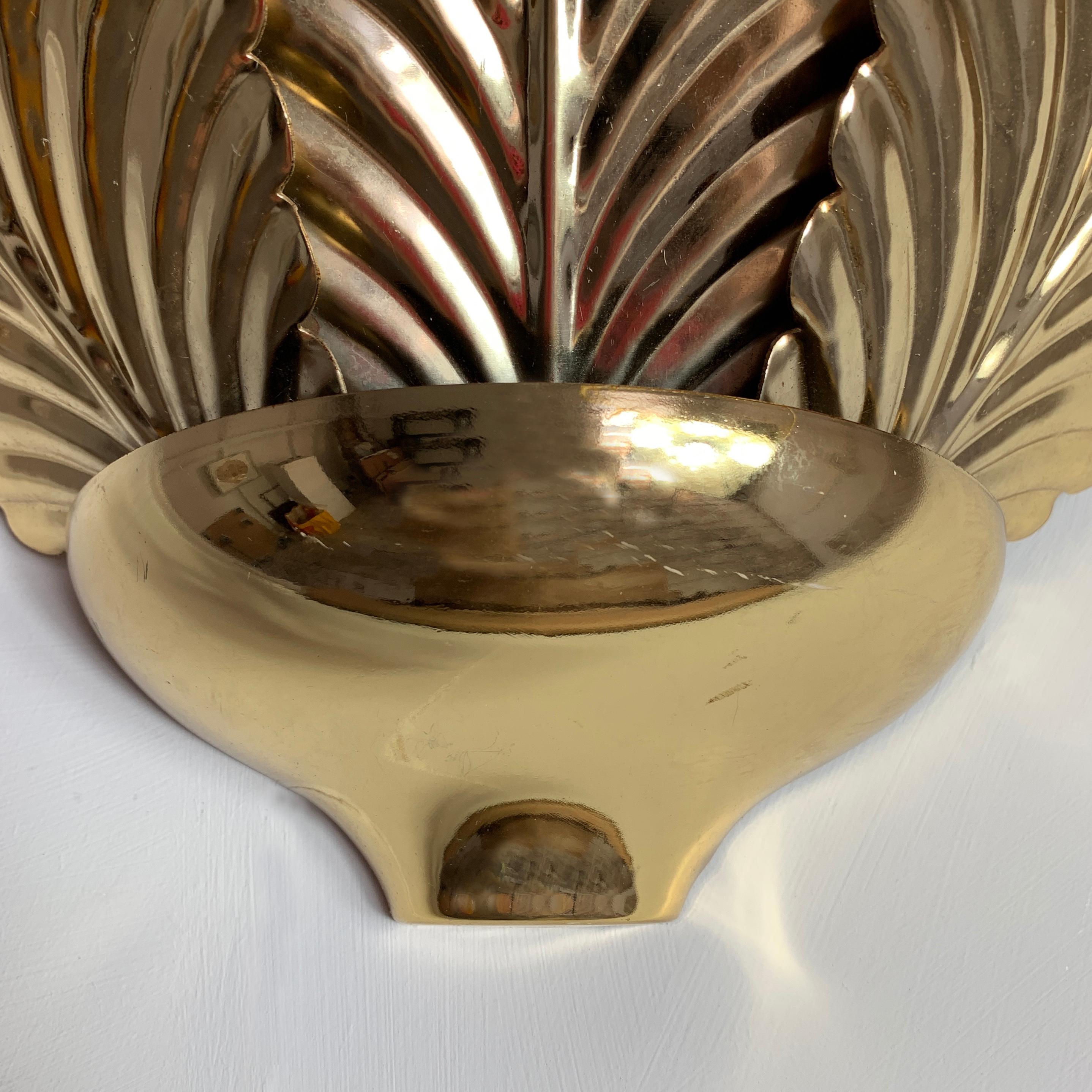 Gold palm leaf wall sconce uplighter.
1980s.
3 large shiny gold metal palm leaves sit inside a gold cup shaped base.
Behind the leaves a single E27 bulb holder is hidden.
There is a bar with 2 hanging hooks on the back to attach to the
