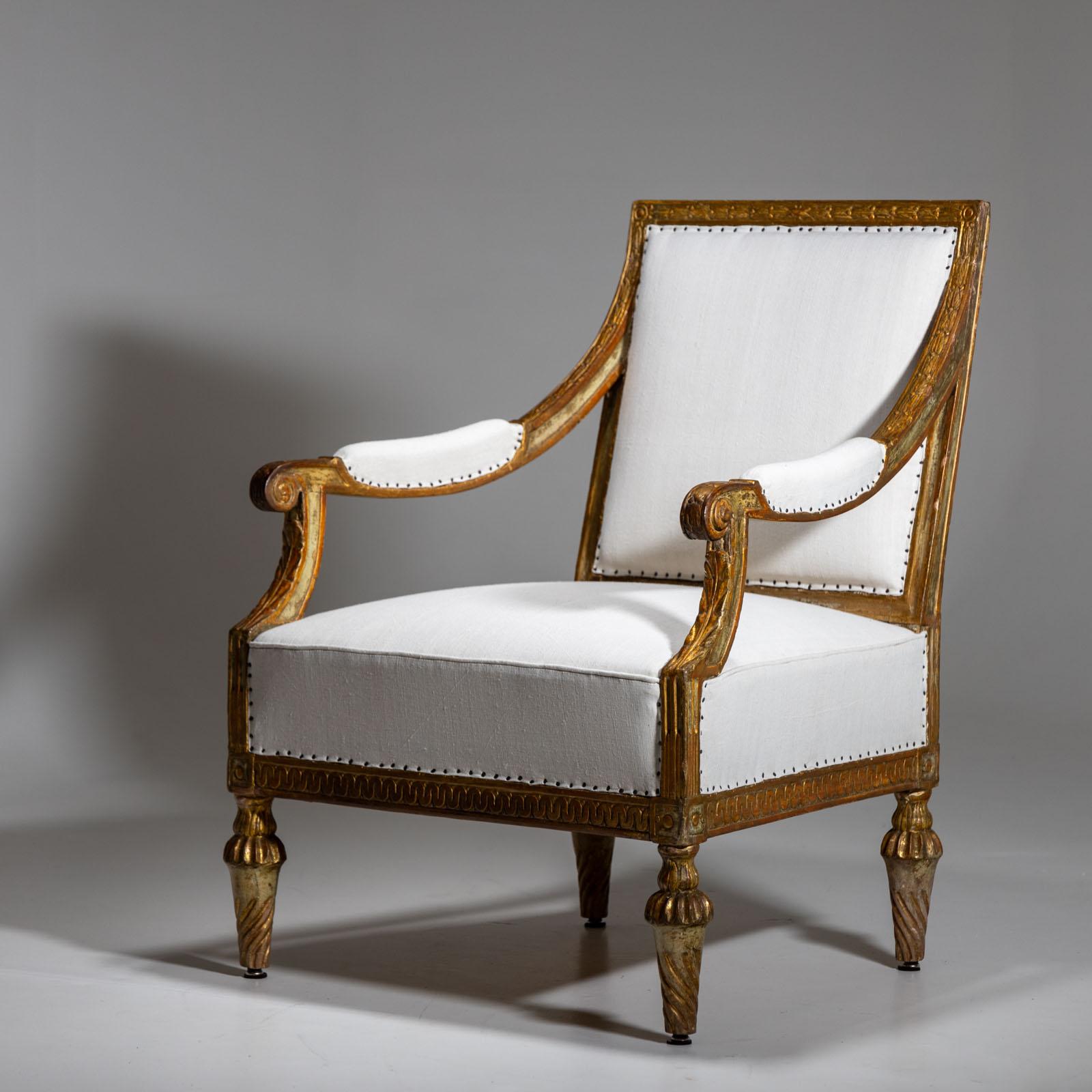 Large gold-patinated Louis Seize armchair on turned-channeled legs and scalloped band on the frame as well as carved leaf decorations on the armrests and backrest. The armchair has a wide seat and the backrest and armrests are also upholstered. The
