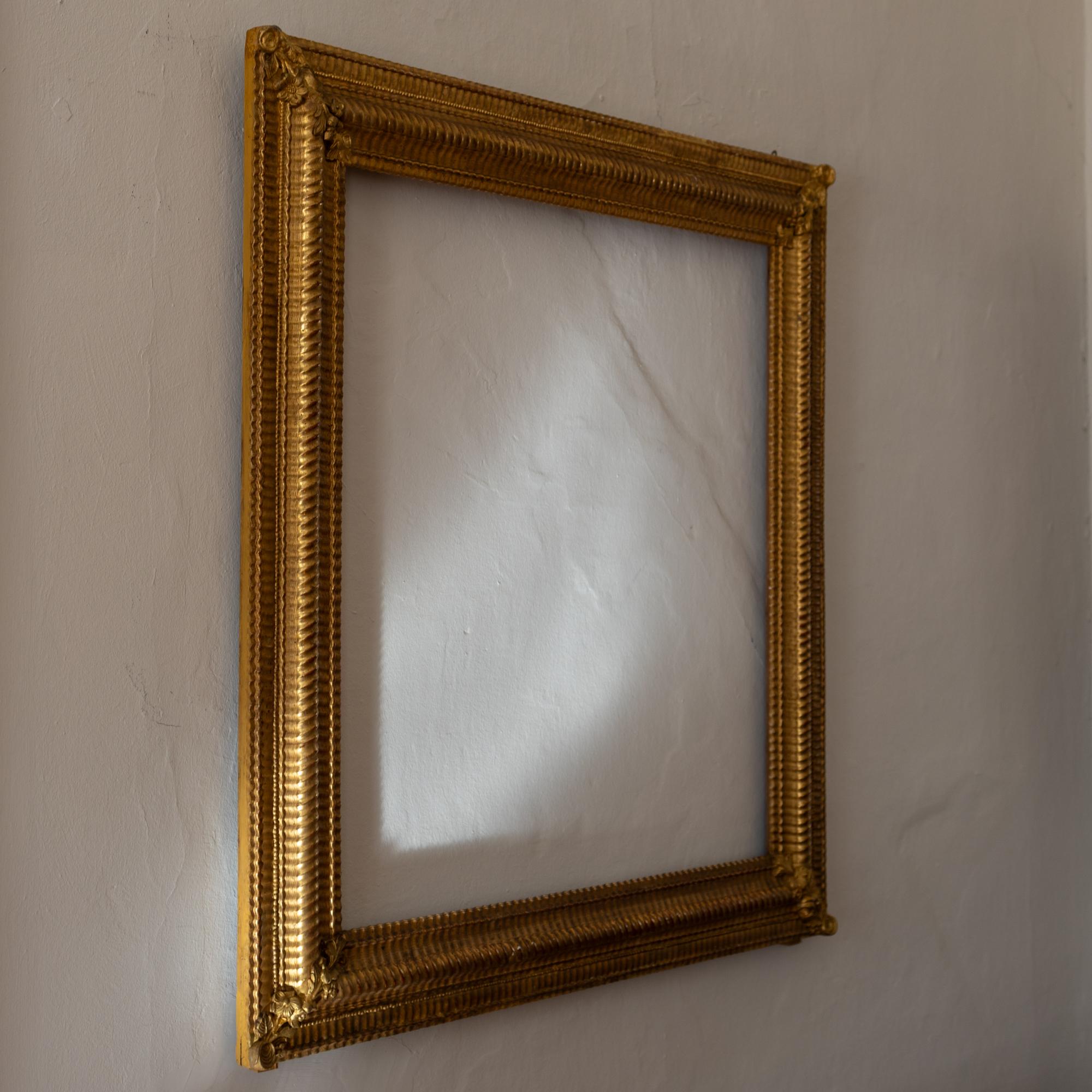 Large mirror frame made of gold patinated and stuccoed wood with floral decorations on the corners. and grooved decorations on the profiled moldings.