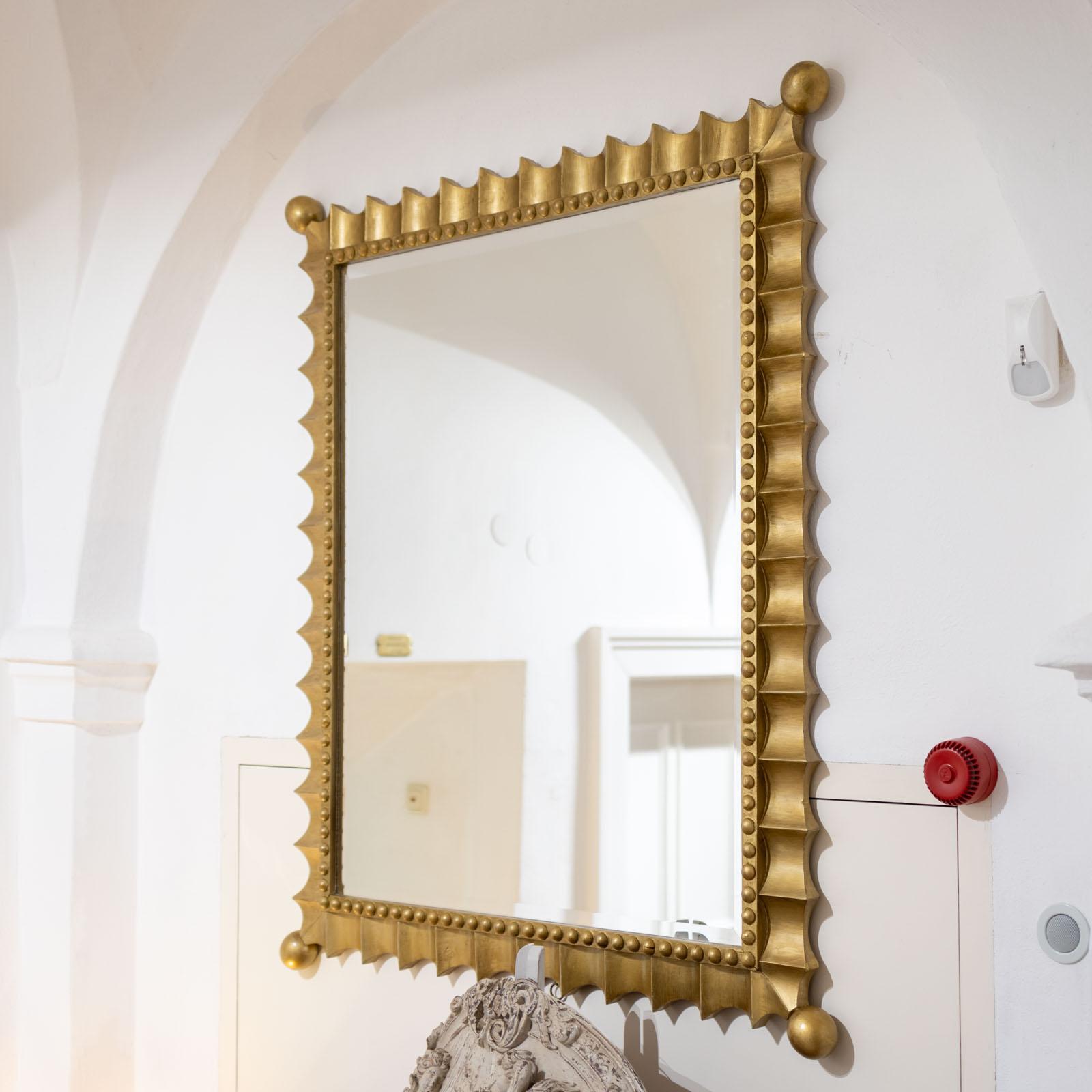 Großer Wandspiegel in einem goldpatinierten Rahmen mit gewelltem Rand und Perlendekor. Die Ecken enden in Kugeln. Die goldene Patina ist in gutem, leicht beriebenem Zustand.