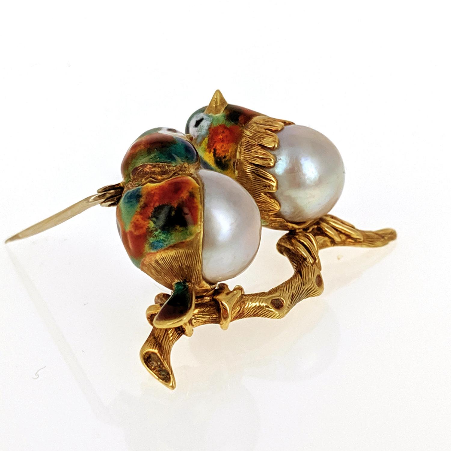 This sweet pin brooch was designed as two lovebirds perched on a branch with white pearl bodices and accented with multi-colored enamel. It is mounted in 18 karat yellow gold.
