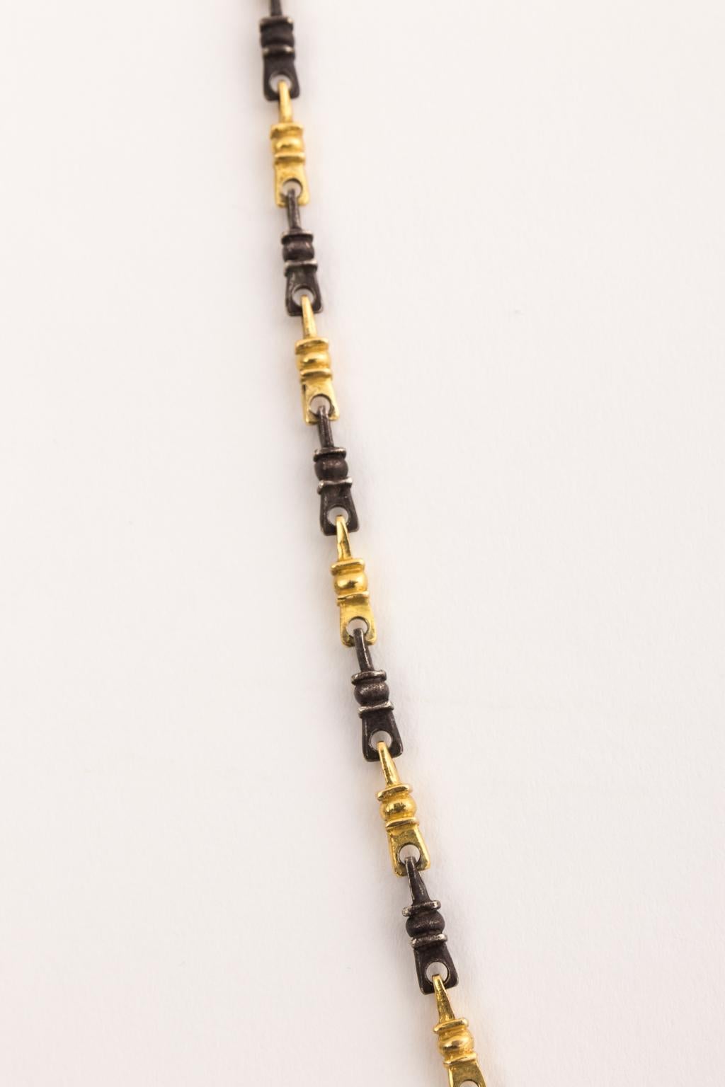 Circa late mid-20th century handmade necklace which consists of an 18 karat gold and ebonized chain holding a rectangular 18 karat gold pendant. The pendant is hand carved with ebonized gold and depicts a figure.
