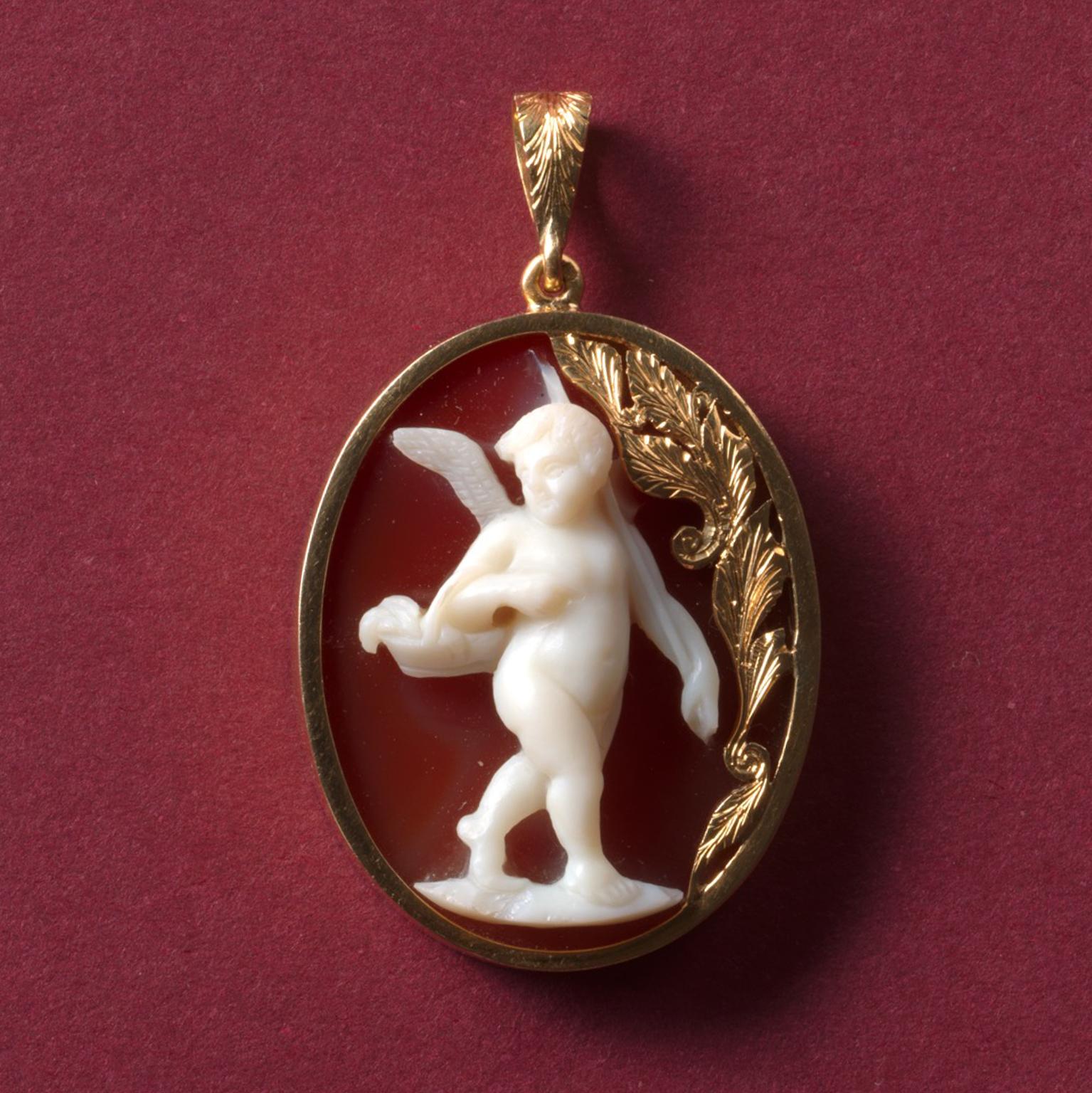 A large oval 18 carat yellow gold pendant featuring a beautiful neoclassical cameo of Amor, god of love, with to its right an engraved floral gold decoration which follows the same engraved eye of the pendant, the cameo is 19th century and the gold