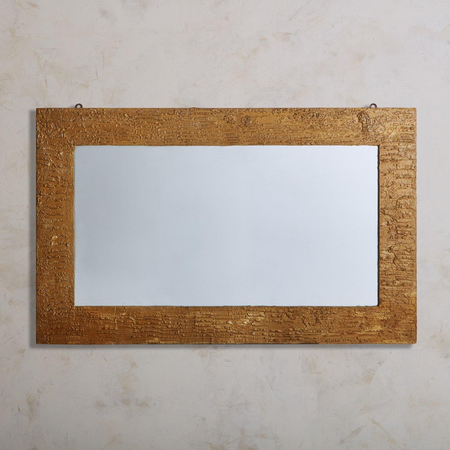 A Mid-Century Italian wall mirror featuring a rectangular textured plaster frame with a gold finish. This mirror has a wooden backing and hardware for hanging. Sourced in Italy, 1970s.

