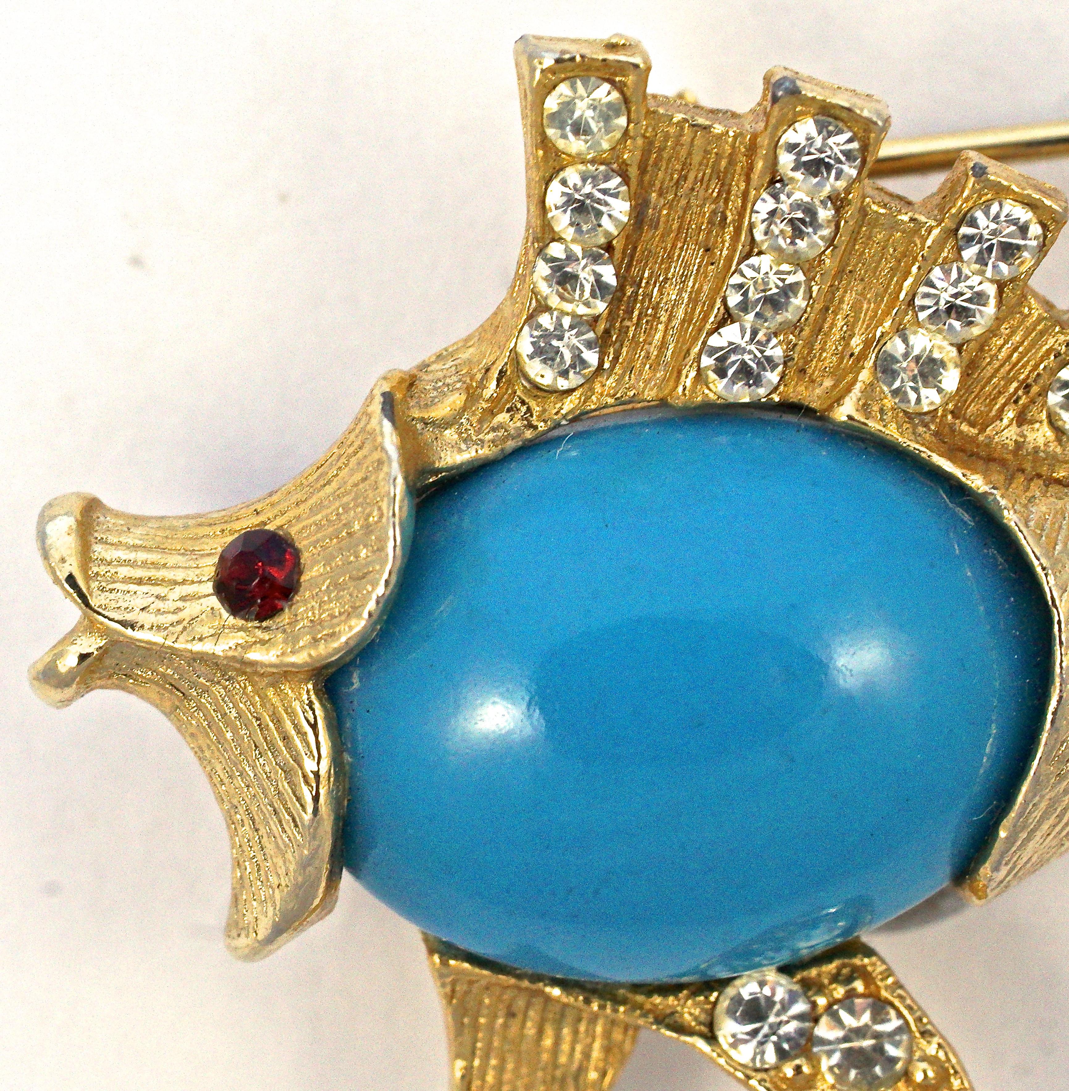 Fantastic textured gold plated figural fish brooch with a red rhinestone eye. The brooch features a mid blue belly and is embellished with clear rhinestones. Measuring maximum width 5.2cm / 2.05 inches by length 3.2cm / 1.26 inches. There is some