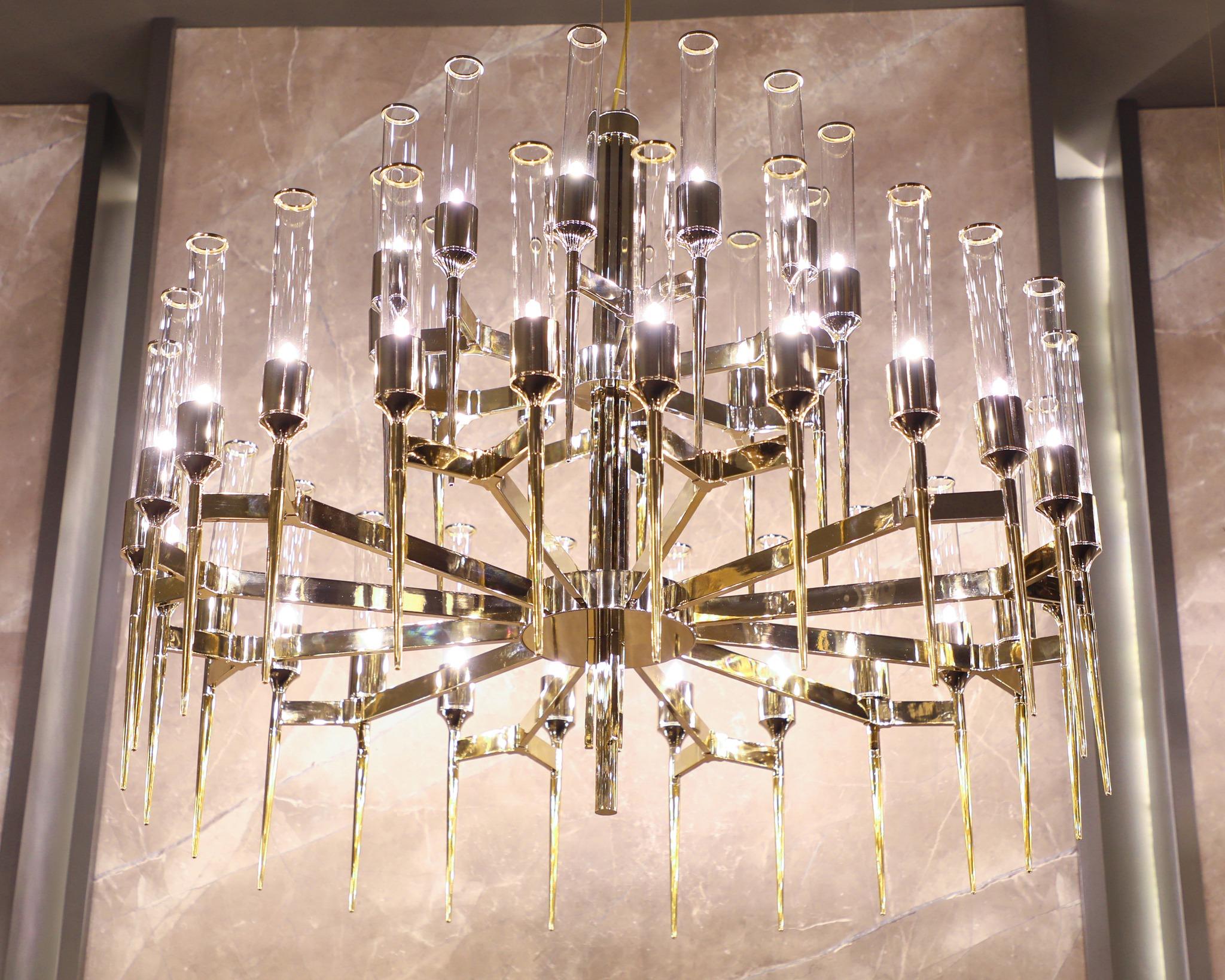 Hecho a mano con latón chapado en oro, sus fuertes líneas crean un movimiento fluido y orgánico con delicados tubos de latón que complementan a la perfección los elementos de cristal transparente. Si se observan de cerca, los tubos alargados se