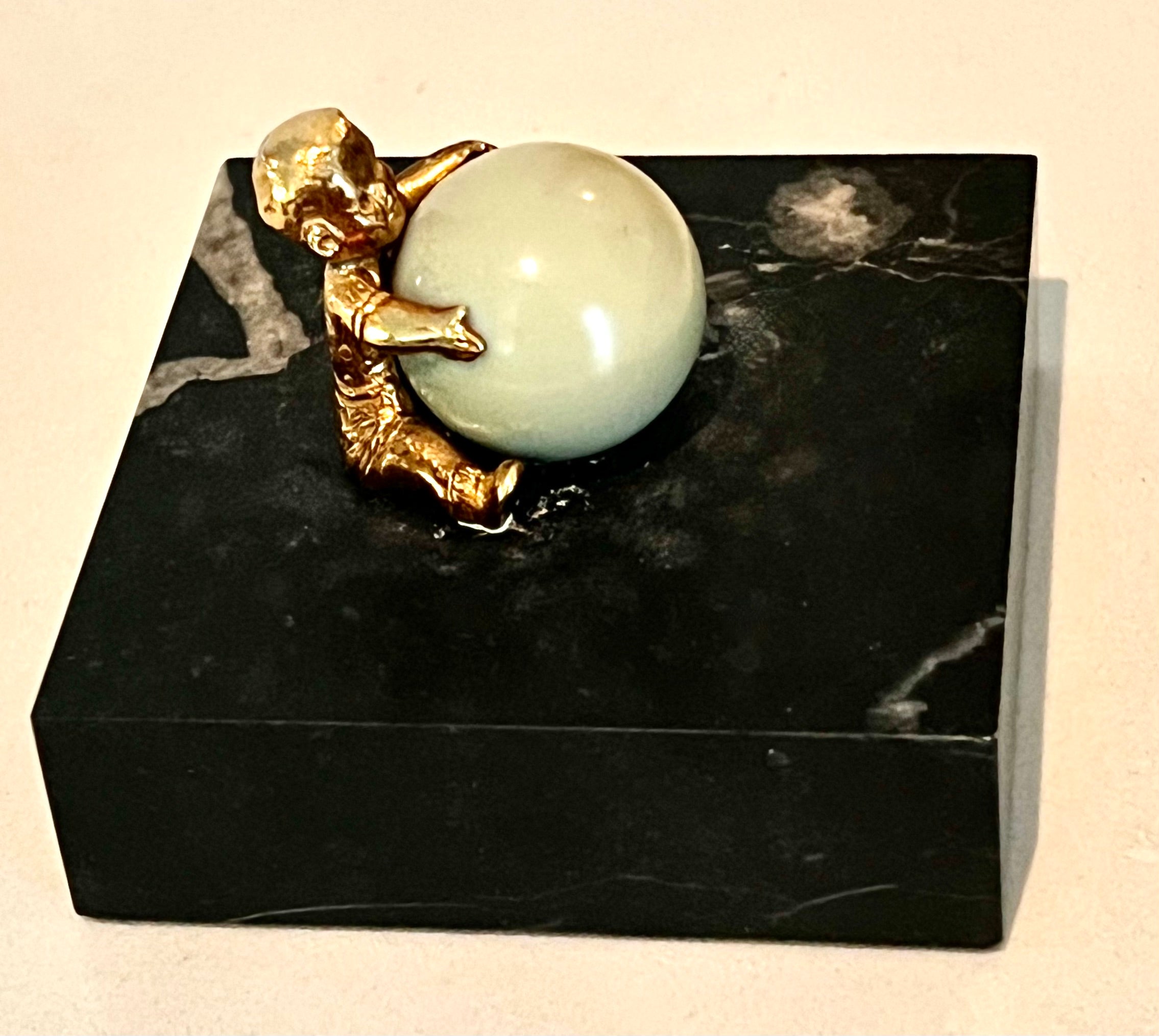 A square Carrara Marble base with a Gold Plated child holding a large Jade Sphere.

The piece is unique and different - a compliment to many spaces.  Works well on a desk or work station.  Also a compliment to a Childs room on a shelf or used as a