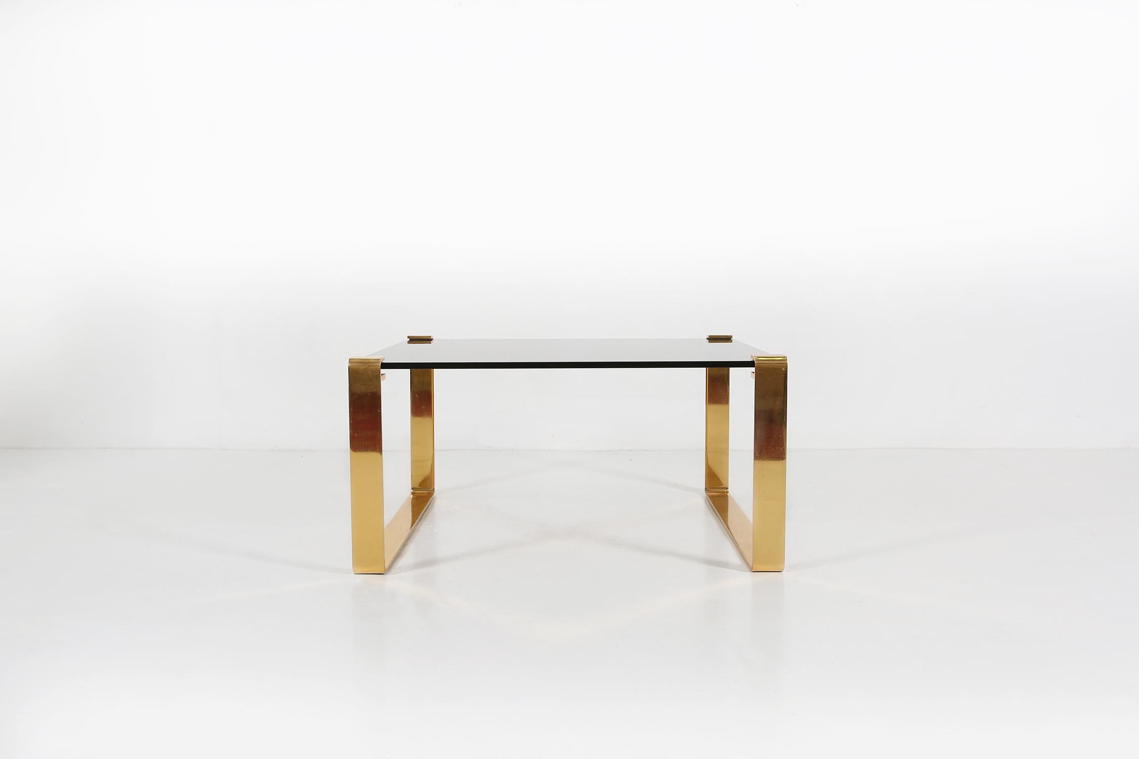 Coffee table made by two gold plated metal legs and a smoked top.
  