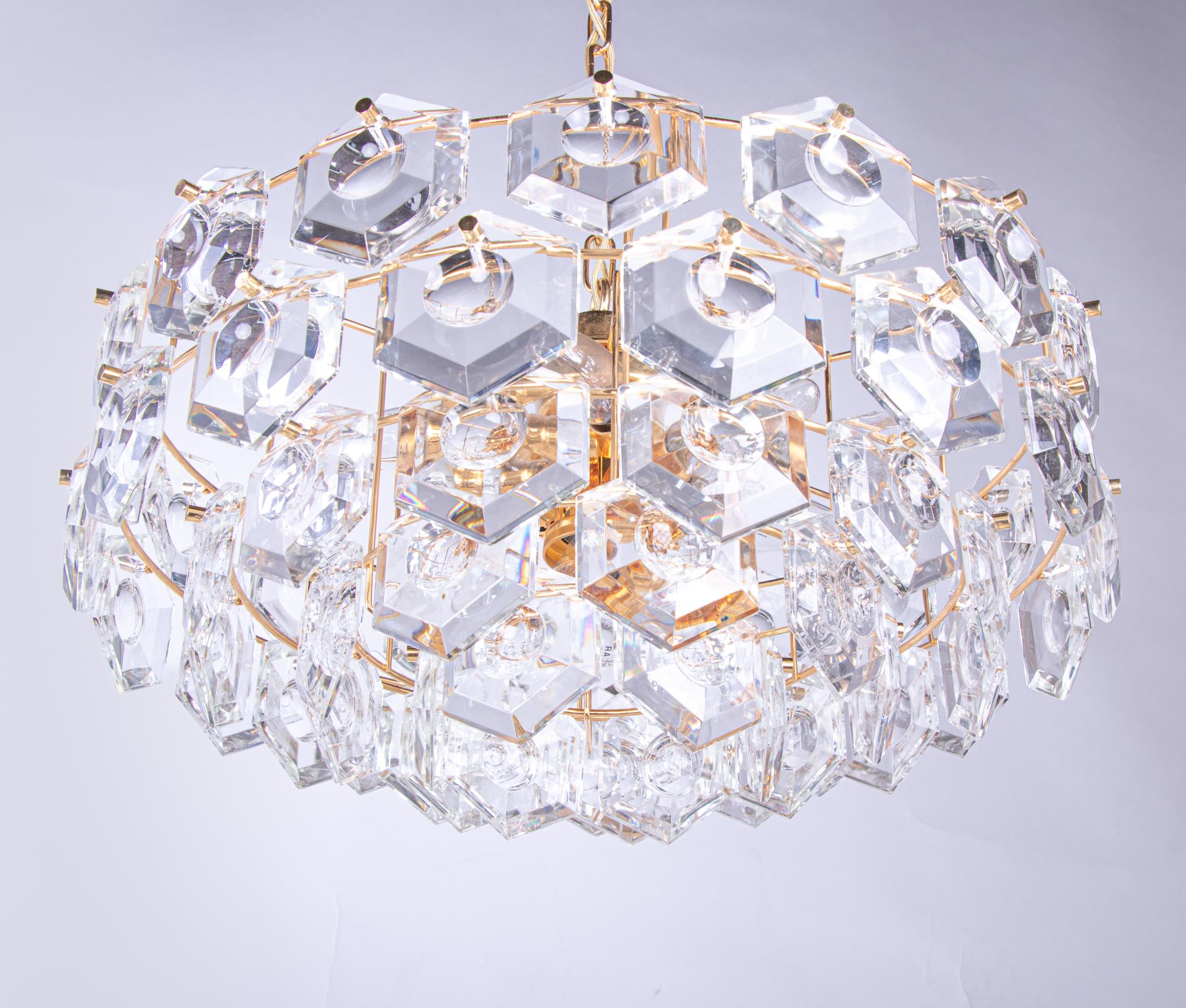 Elegant lens chandelier with hexagonal faceted crystals on a gold-plated brass frame. Crystal elements resembles lenses. Heavy design. Chandelier illuminates beautifully and offers a lot of light. Gem from the time. With this light you make a clear