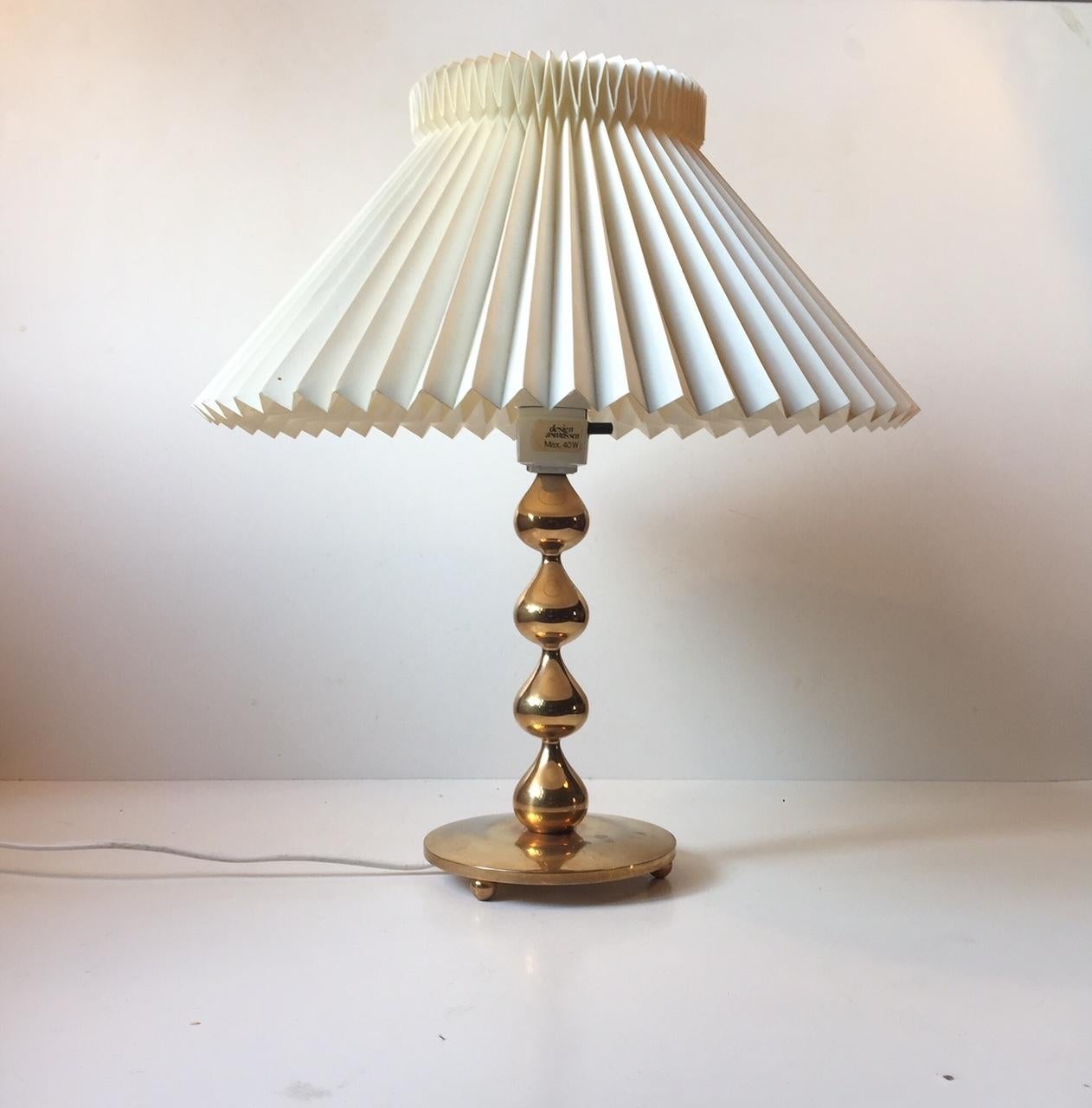 This gold-plated table light is composed of 4 intervened drops. It was designed during the 1960s by Hugo Asmussen in Denmark. This is an example from the late 1970s. The base/foot of the light shows ware, patina and has been polished. The shade is a