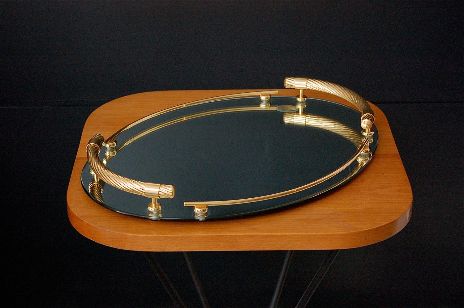 Oval mirrored serving tray in tempered glass with 6mm thickness. 24-karat gold-plated handles and bars are mounted along the edge of the tray. It has quality finishes like the rope twist effect and leather covered base. To use as a drinks tray or