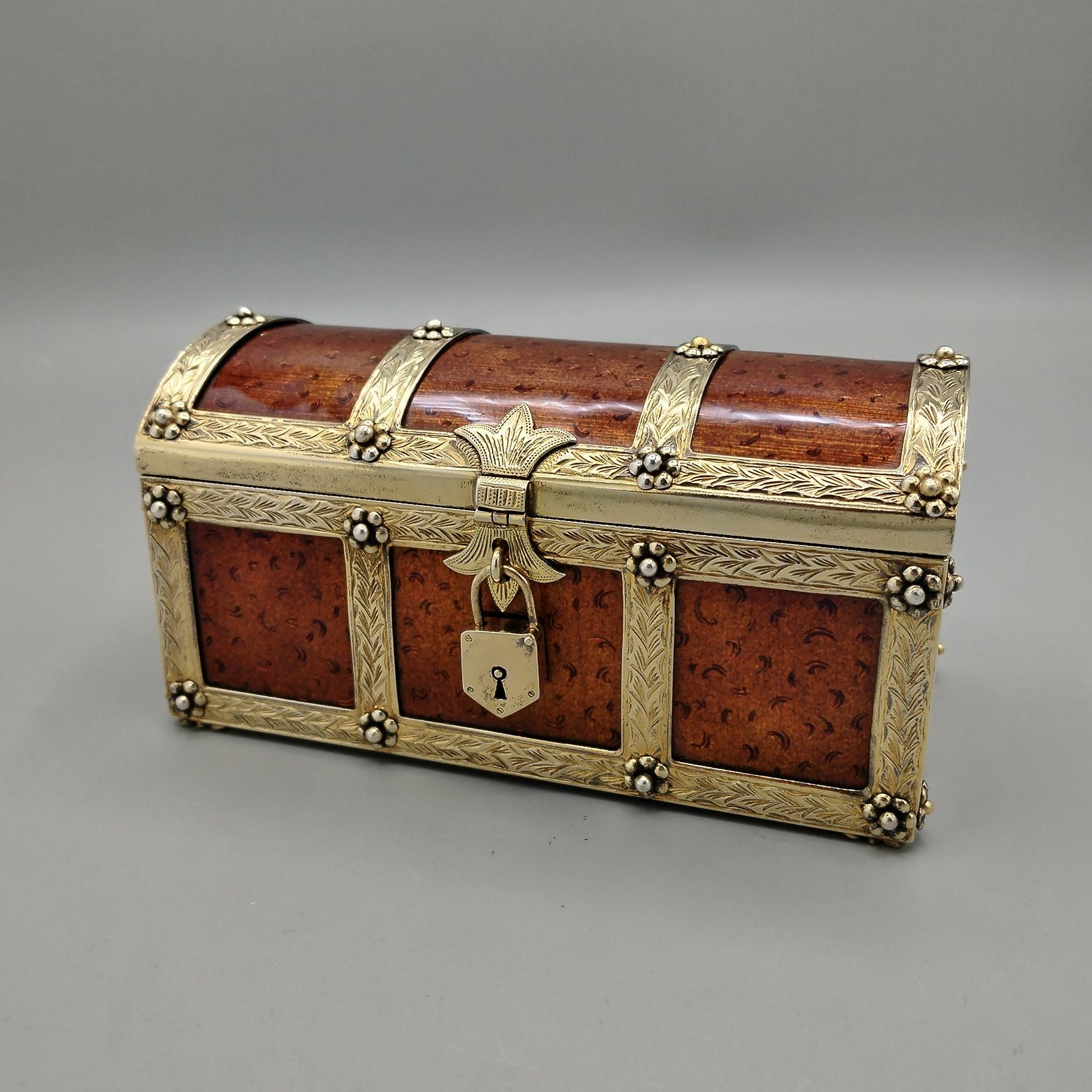 Boîte à bijoux entièrement réalisée à la main en argent sterling plaqué or et en émail de feu brun en forme de coffre.
La forme est rectangulaire avec un couvercle à charnière convexe.
Le cadre de la boîte à bijoux a été gravé et enrichi de roses,