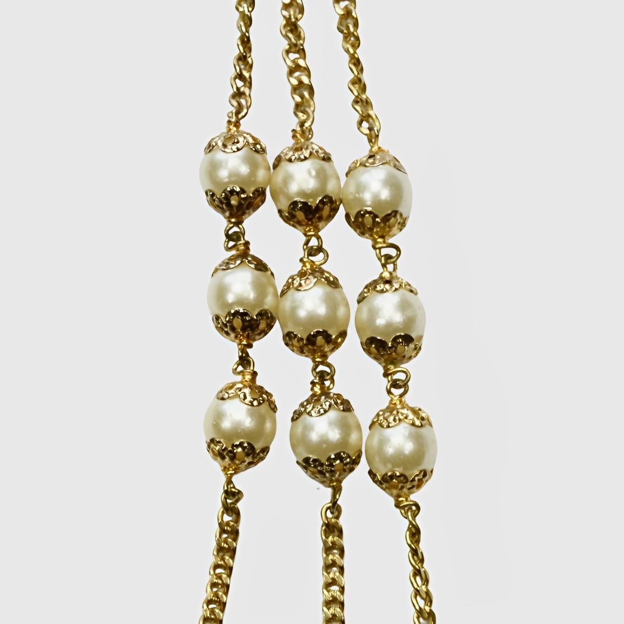 Precioso collar de cadena de tres vueltas chapado en oro, con perlas de imitación y eslabones adornados. La longitud más corta es de 57 cm. El baño de oro y las perlas de imitación están desgastados.

Este inusual collar es de la década de 1950. 