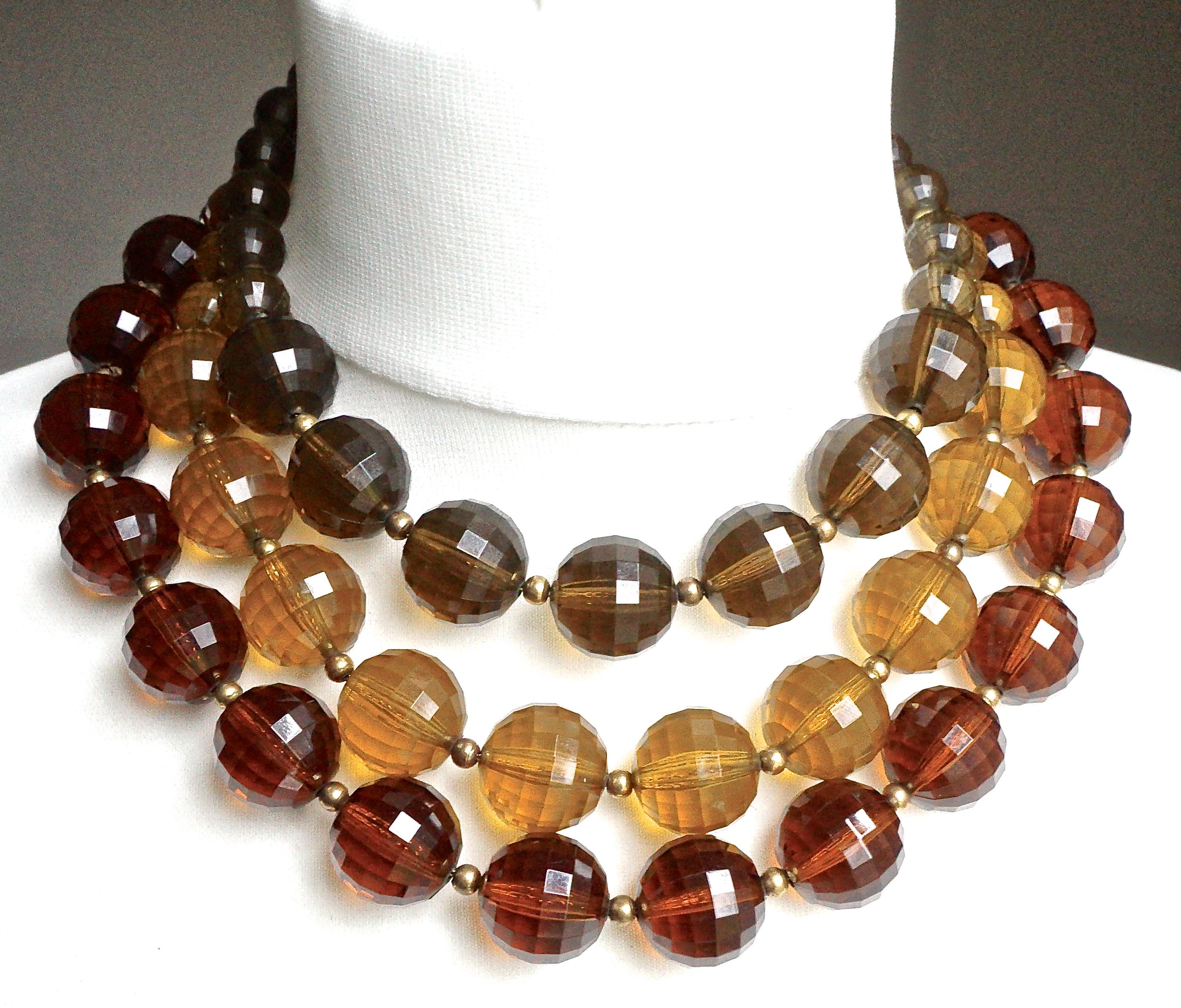 Gold plated necklace featuring three strands of faceted plastic beads in warm mid brown, golden, and olive. They are strung on chain, and there are small gold beads between each larger bead. The necklace has a large faceted glass clasp in a lovely