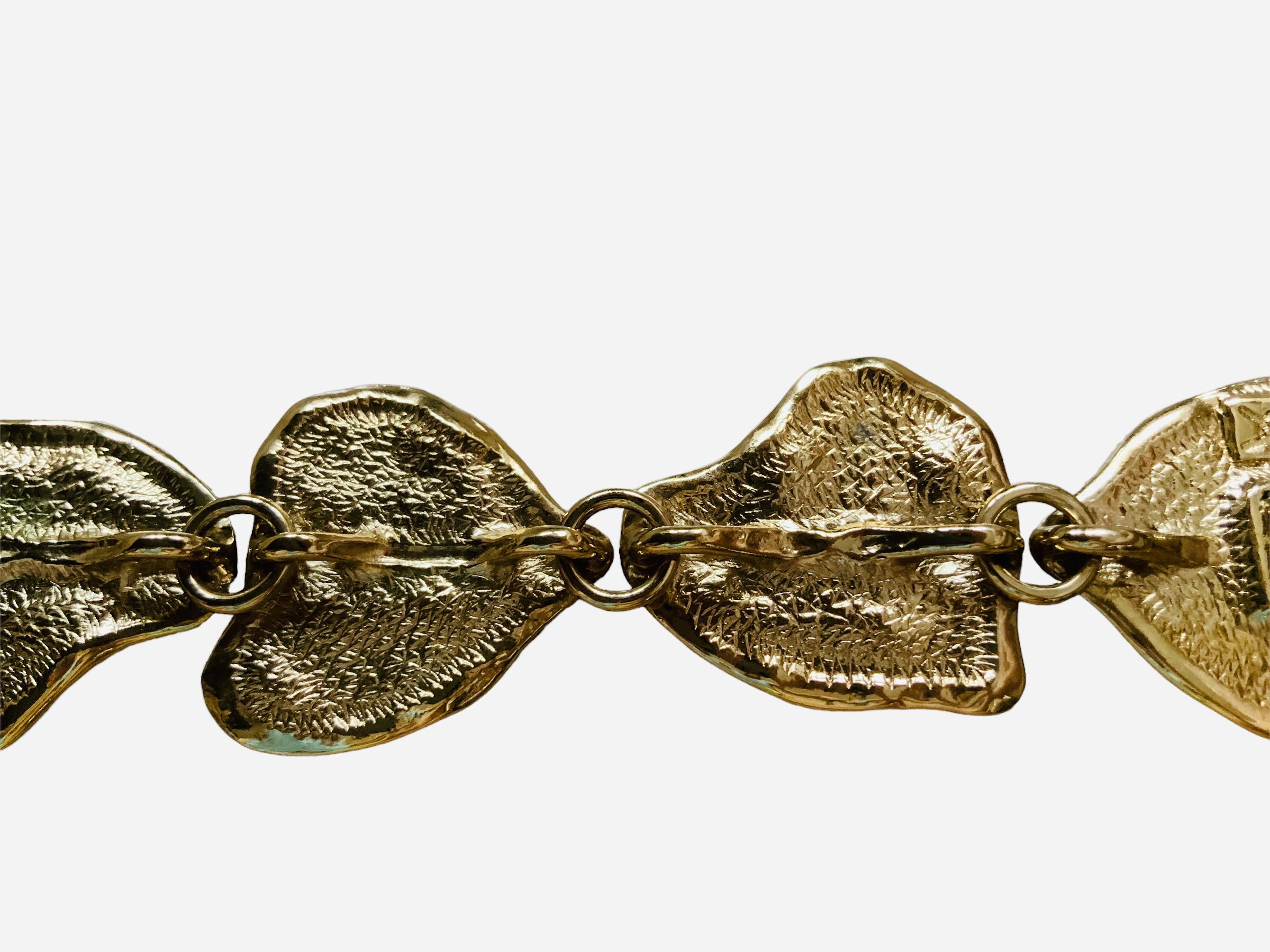 This is a Yves Saint Laurent gold plated link bracelet. It depicts seven asymmetrical rock texture hearts link bracelet. It closes with a hidden clasp box. It is signed with the YSL logo in the back of the clasp box.