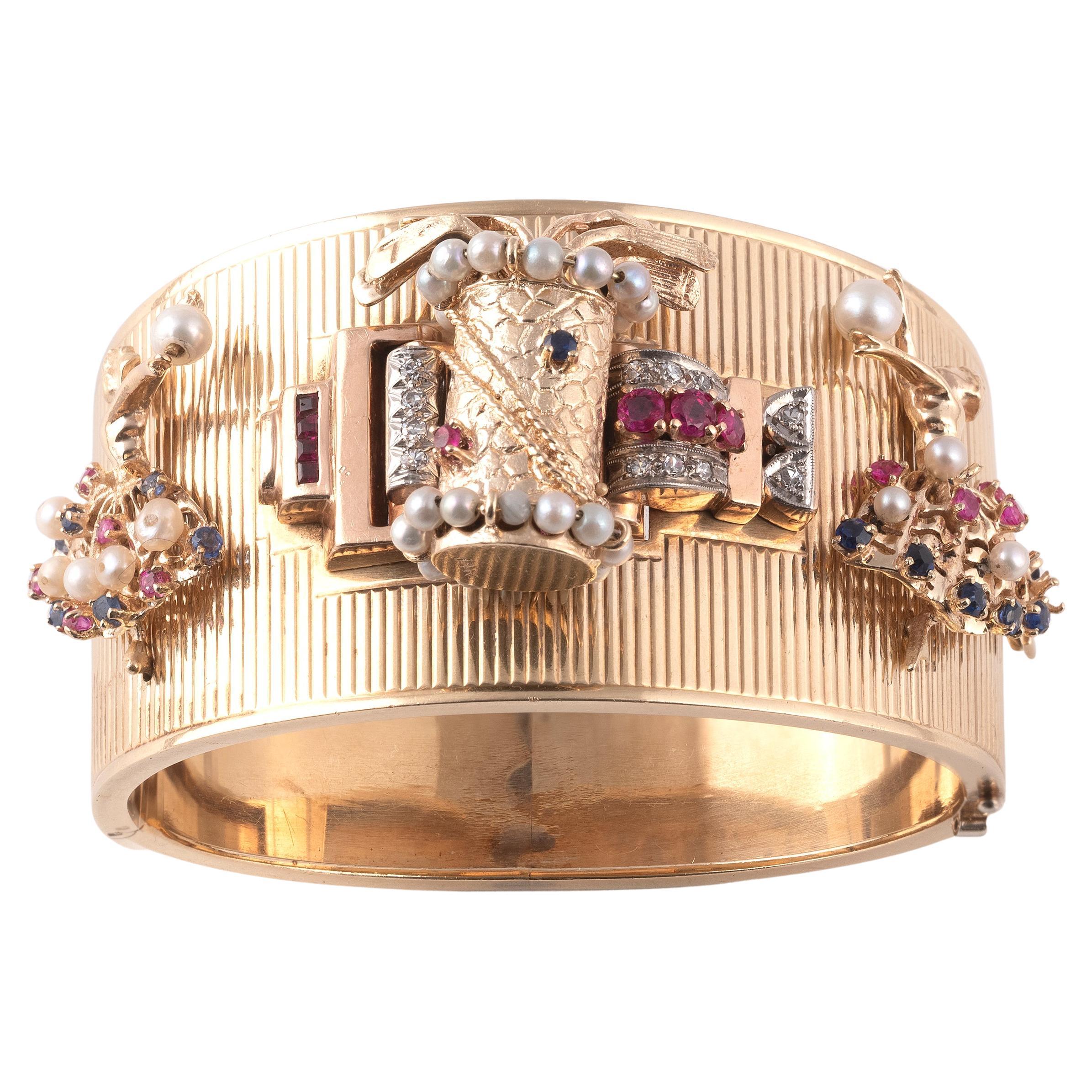 Il braccialetto-bangle in oro testurizzato è decorato con tre charme raffiguranti due ballerine ai lati e una sacca da golf al centro, con diamanti, rubini, zaffiri e perle di vario taglio.

Peso circa 76gr.

Circonferenza interna: 17,7