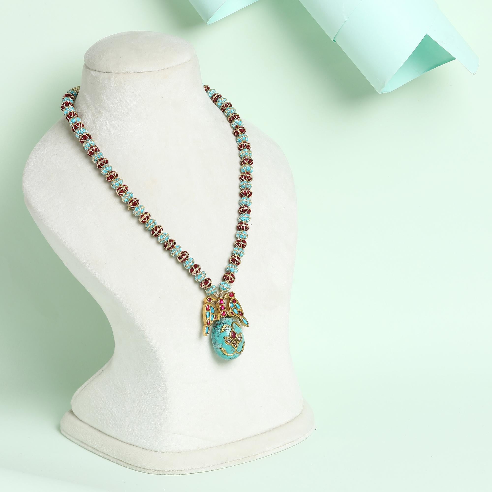 Strung on a  hand woven necklace of golden silk thread with artistic knots, this Turquoise stone bird motif pendant is encrusted with Polki diamonds and rubies. 