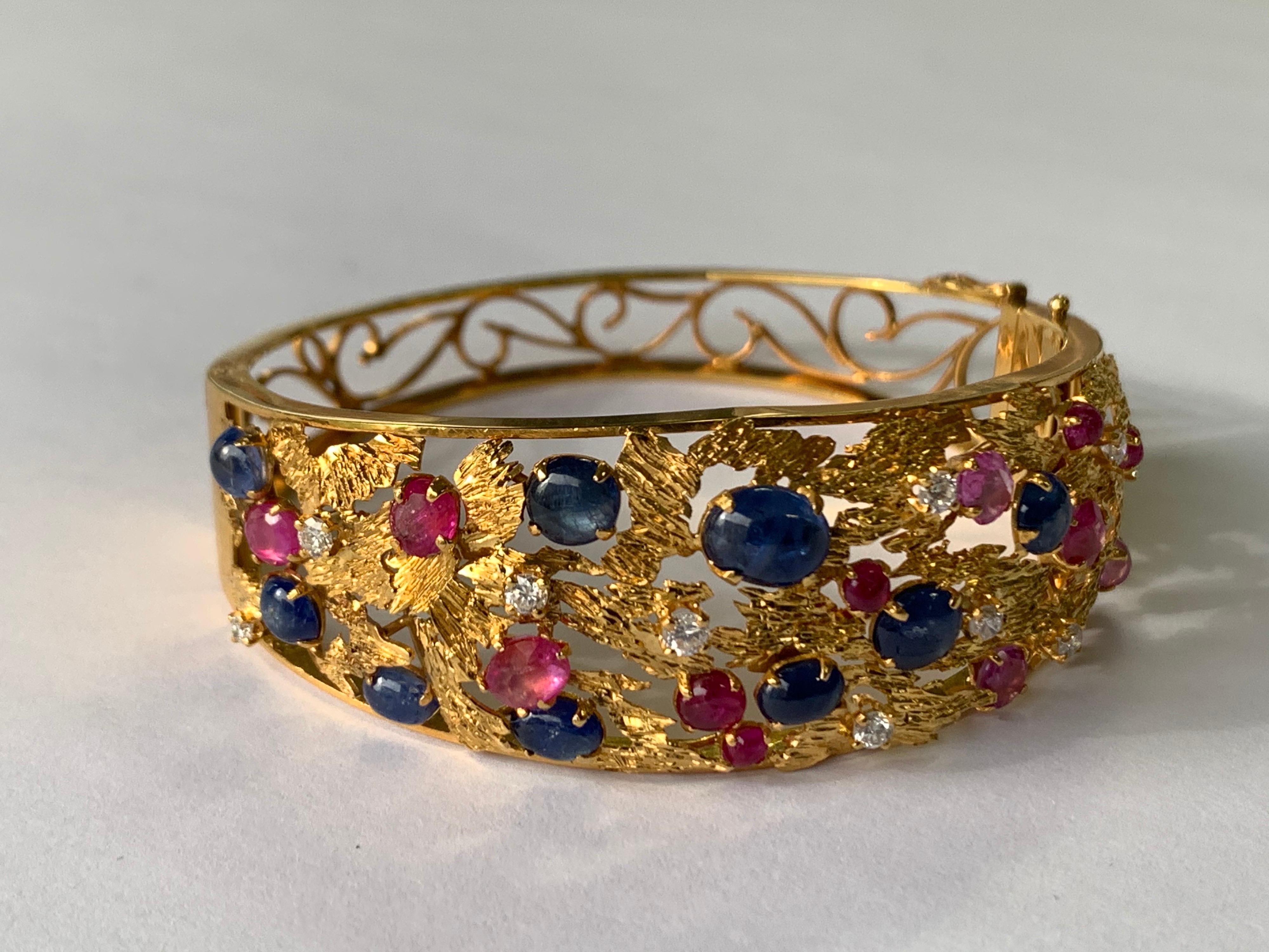Stunning 14K Yellow Gold Retro Bangle weighing 27.09 grams. 

The Bracelet consists of 10 Natural Round Brilliant Diamonds (colorless, VS-SI, appx 0.60 carats), 12 Natural Rubies (faceted&Cabochon, appx 2.10 carats), and 9 natural Cabochon Sapphires