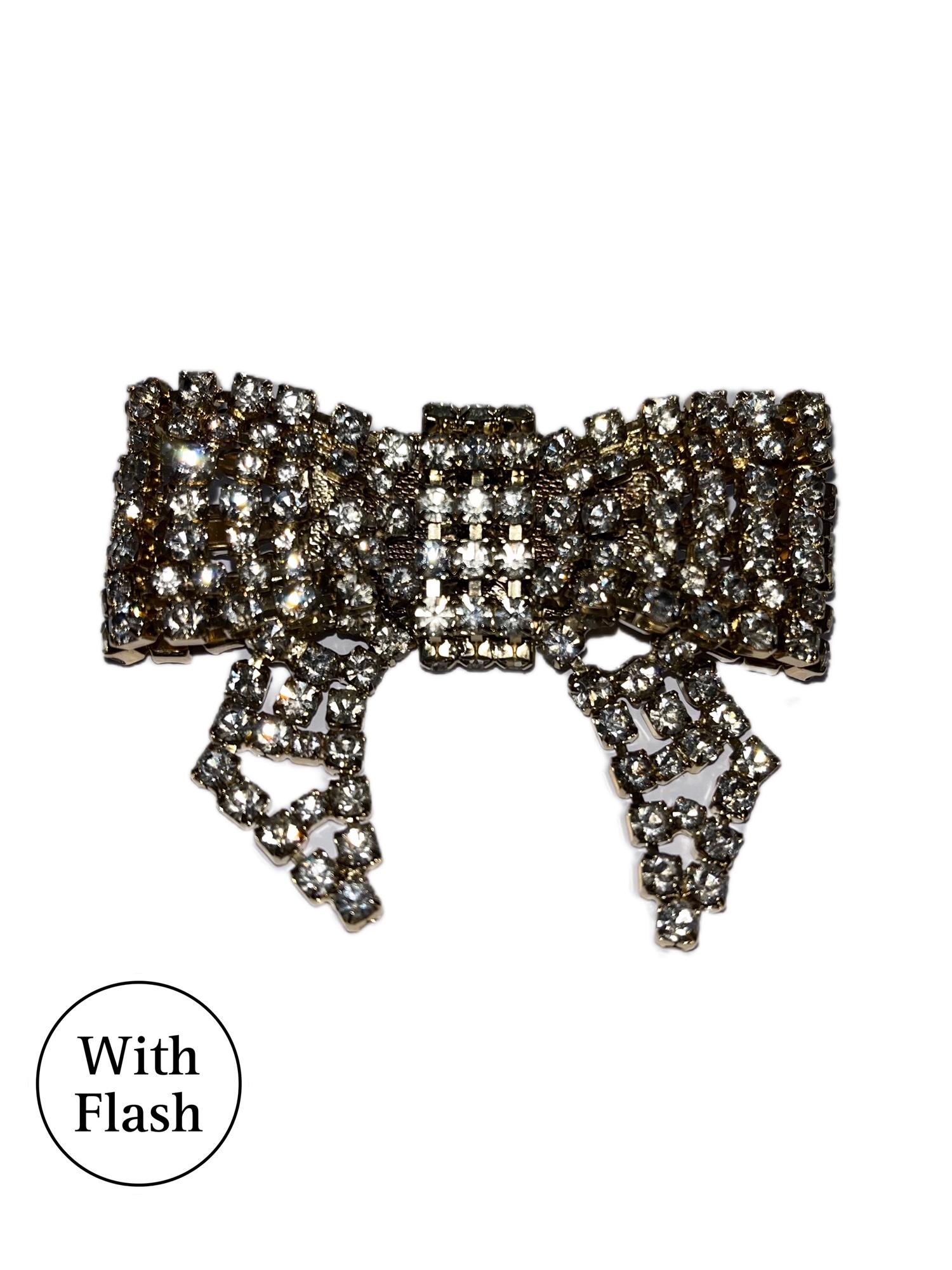 This simple yet astonishing gold-toned brooch is from the creator Daniel Swarovski. The brooch is bow-shaped, with same size square crystal. They are put together as articulated rhinestones. The brooch was never worn before and therefore is in