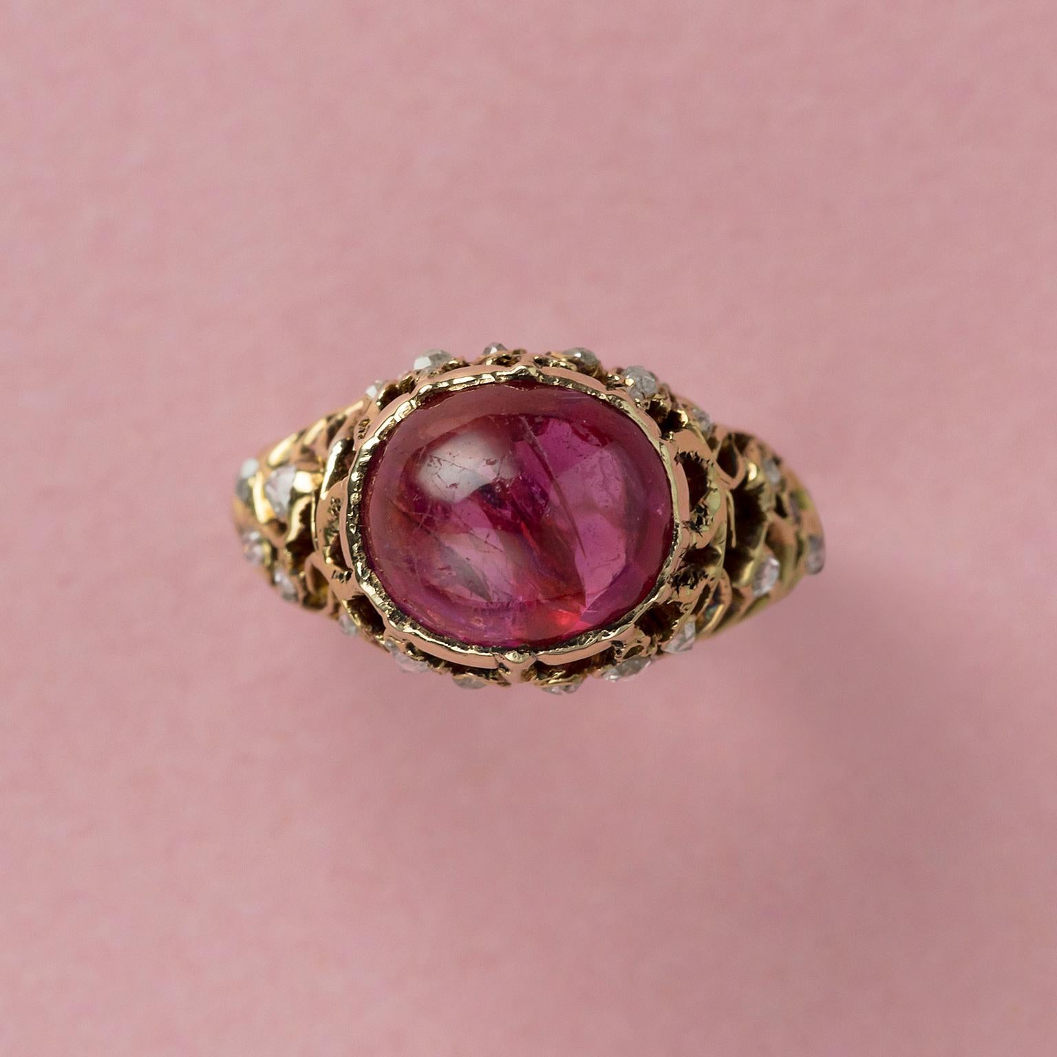 A pretty 18 carat gold ring set with a warm and pretty cabochon cut natural unenhanced red-pinkish Burma sapphire (app. 4.7 carat with certificate) the shank is completely open worked with scrolls that are decorated with rose cut diamonds.

weight: