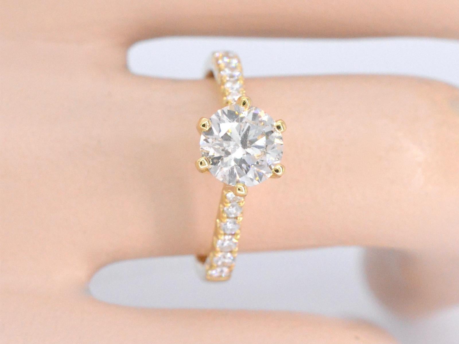 Wir präsentieren einen exquisiten Ring mit einem Primärdiamanten von 1,25 Karat. Dieser Diamant im Brillantschliff hat eine ausgeprägte M-Farbe und einen Reinheitsgrad von SI und bietet ein helles und auffälliges Erscheinungsbild. Der Ring enthält