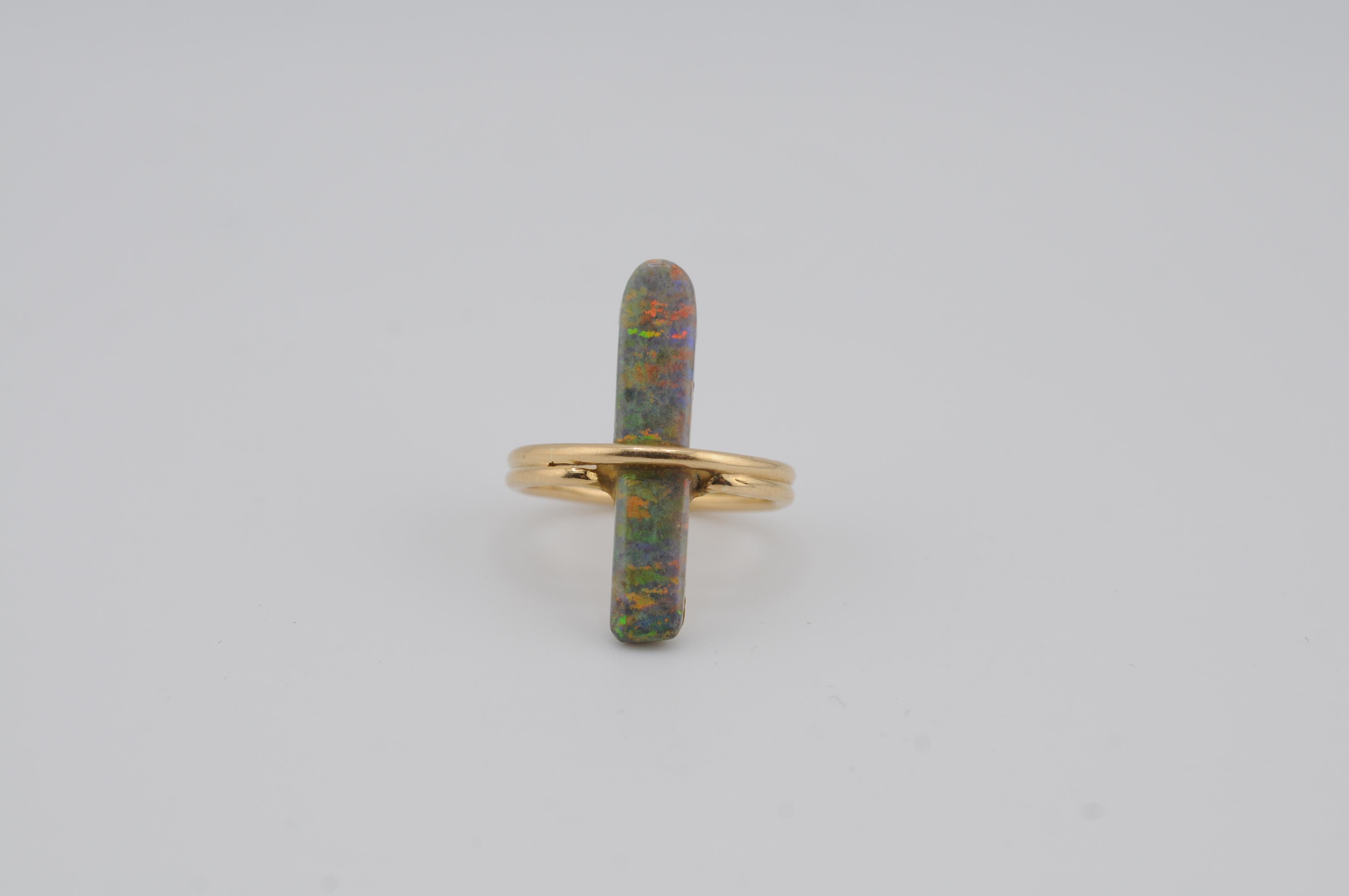 Elegante anello realizzato in oro giallo 18 carati con un opale naturale dal taglio rettangolare con bellissimi giochi di colore. L'opale mostra sfumature mutevoli sotto diverse luci, incastonato in una cornice d'oro pulita e senza tempo. Un pezzo