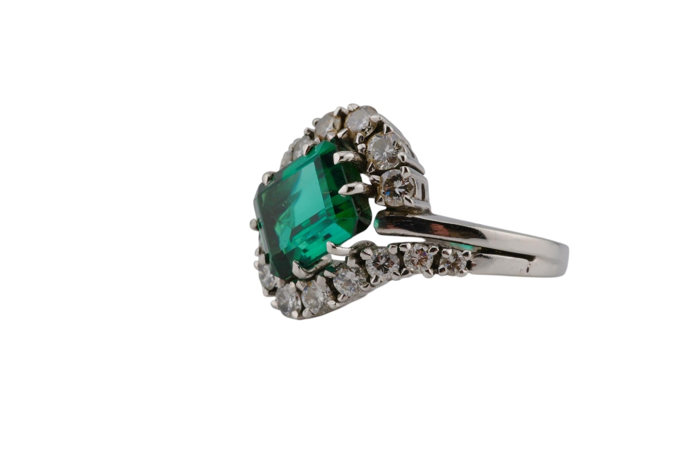 Anello in oro bianco 18 carati con tormalina brasiliana naturale dalla vibrante tonalità verde, circa 4 carati. Circondato da 16 diamanti a taglio brillante, ognuno dei quali pesa tra 0,05 e 0,20 carati circa.

Misura dell'anello EU 56 (US 7). Le
