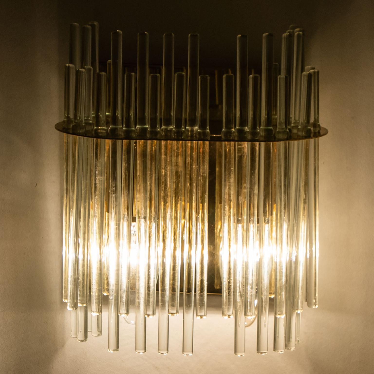 Wonderful high-end wall sconces in the style of Sciolari. With long glass 'tubes' and brass details giving each piece an elegant appearance which refracts the light, filling a room with a soft, warm glow.
The wall sconce has a brass back