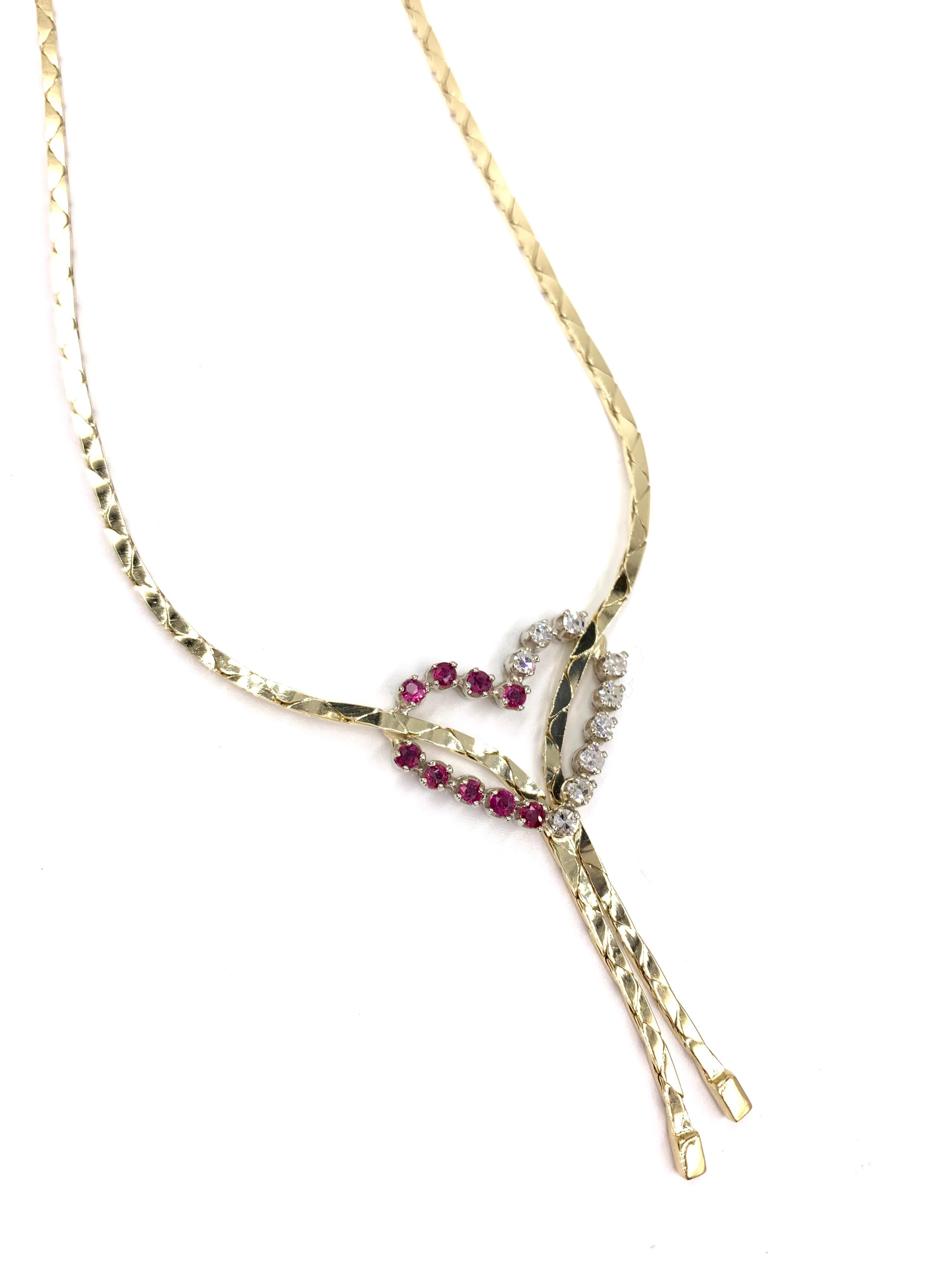 A wearable 14 karat yellow gold lariat style necklace made from a beautiful 1.5mm flat high-polished chain, joining at the center with an open heart pendant featuring 9 round single cut white diamonds and 9 round well saturated rubies. Diamond total