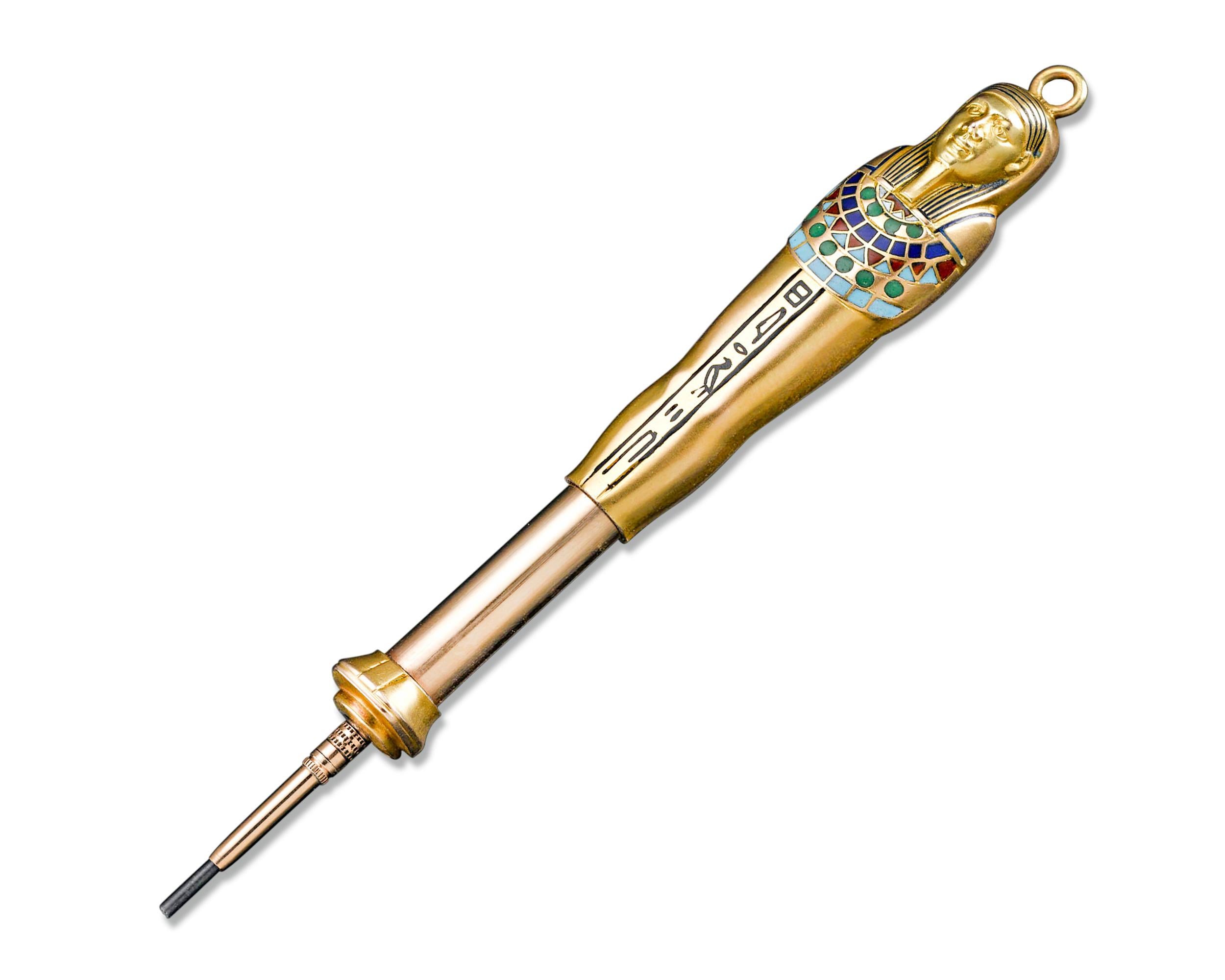 This diminutive Egyptian Revival era gold mechanical pencil takes the form of an Egyptian sarcophagus. Wonderful, natural hardstone inlay and enameled hieroglyphs add elegance and history to this fascinating writing instrument. An attached bail